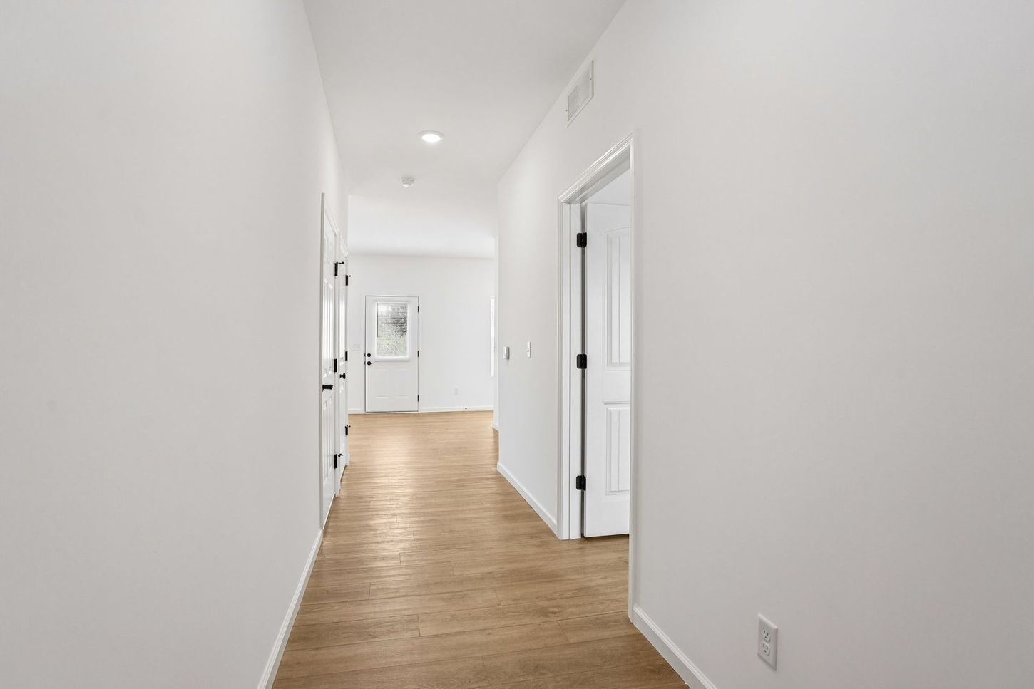 Bright white hallway with wood flooring and open doorways leading into a home interior
