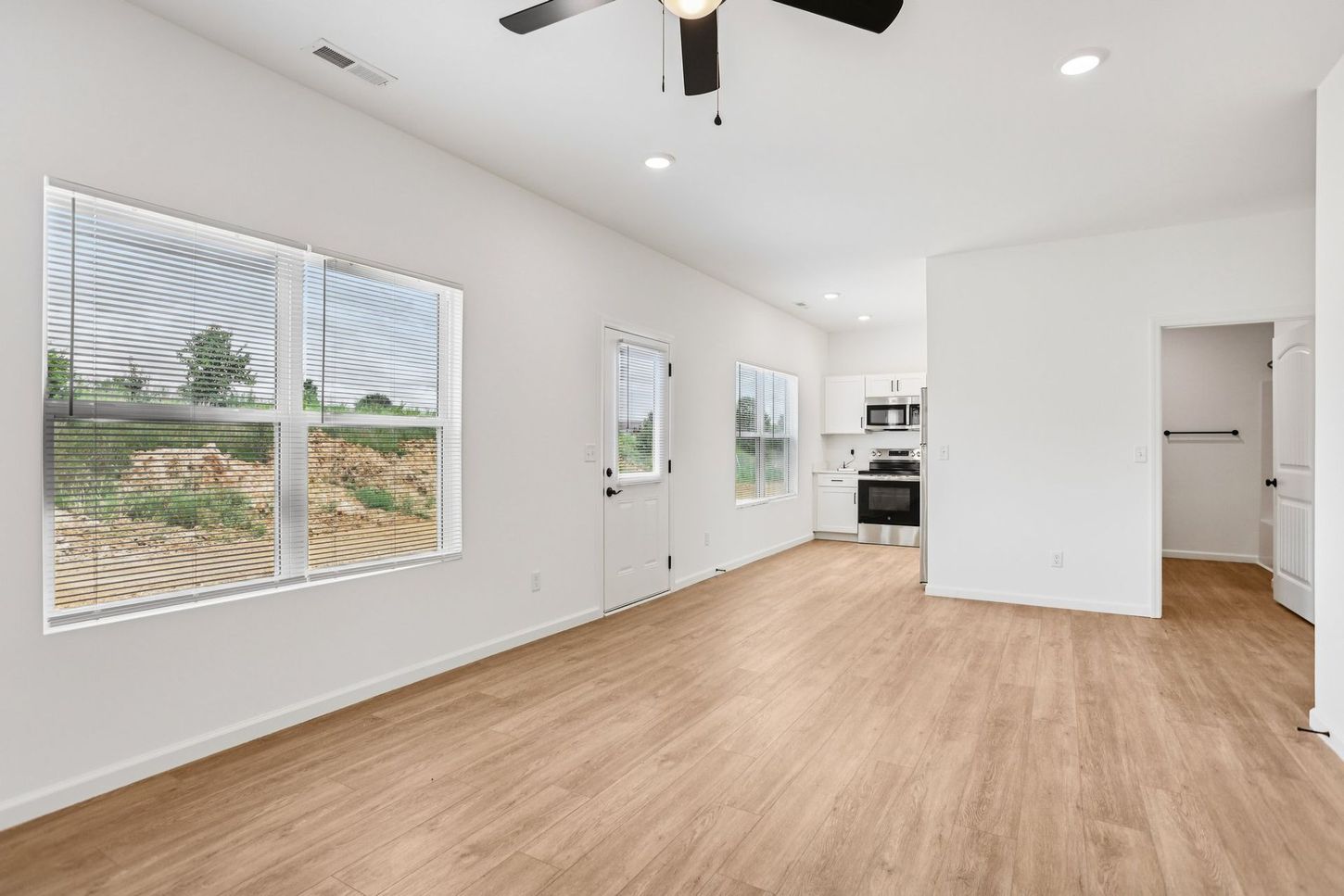 Bright empty room with wood floors, white walls, large windows, and a ceiling fan.