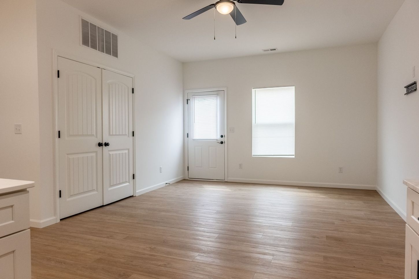Empty white room with wood flooring, ceiling fan, closet doors, and a window with blinds.