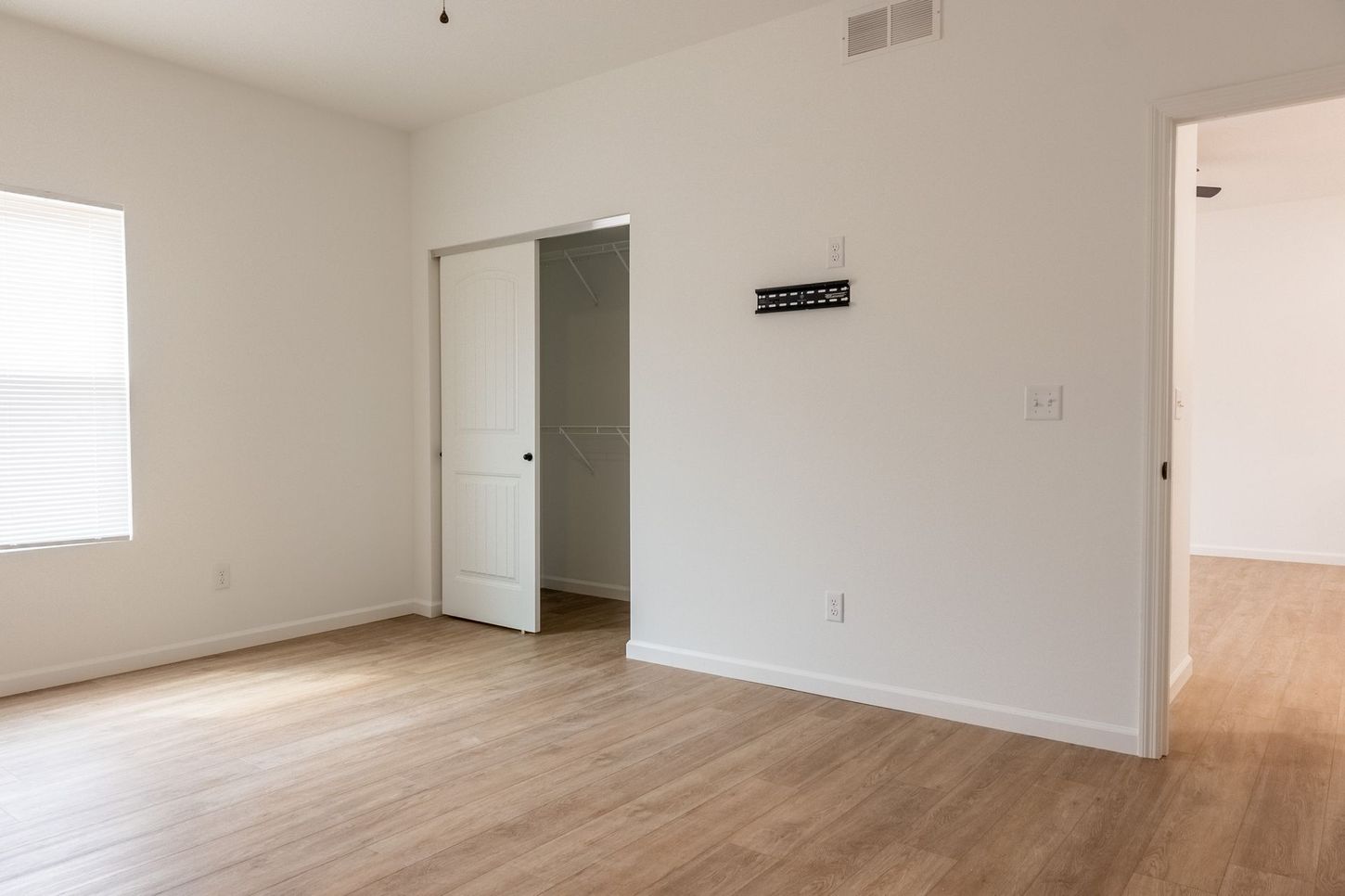 Empty beige room with wood floors, two doorways, and a small window