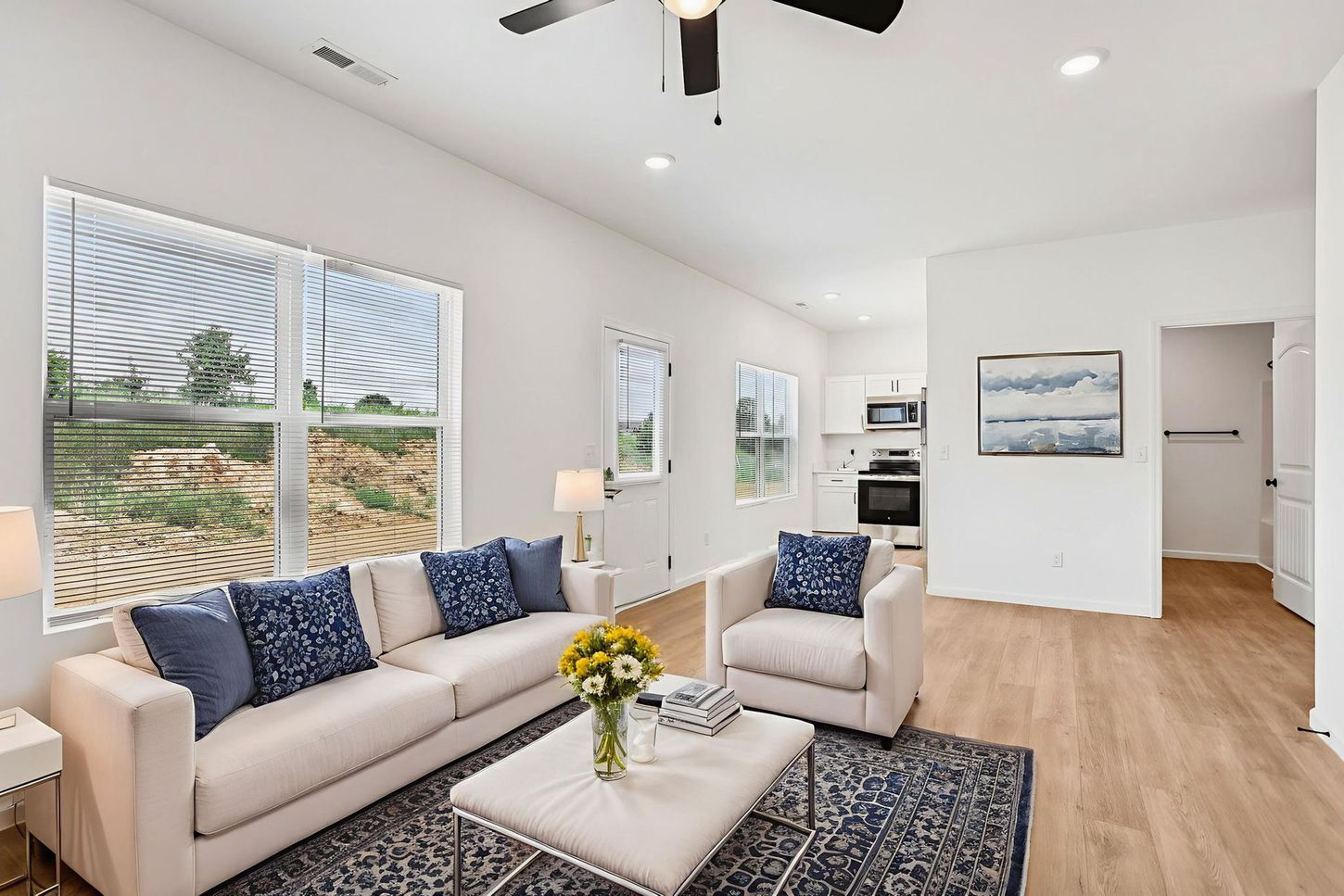 Bright living room with white sofa, blue chairs, coffee table, and large windows overlooking a desert view