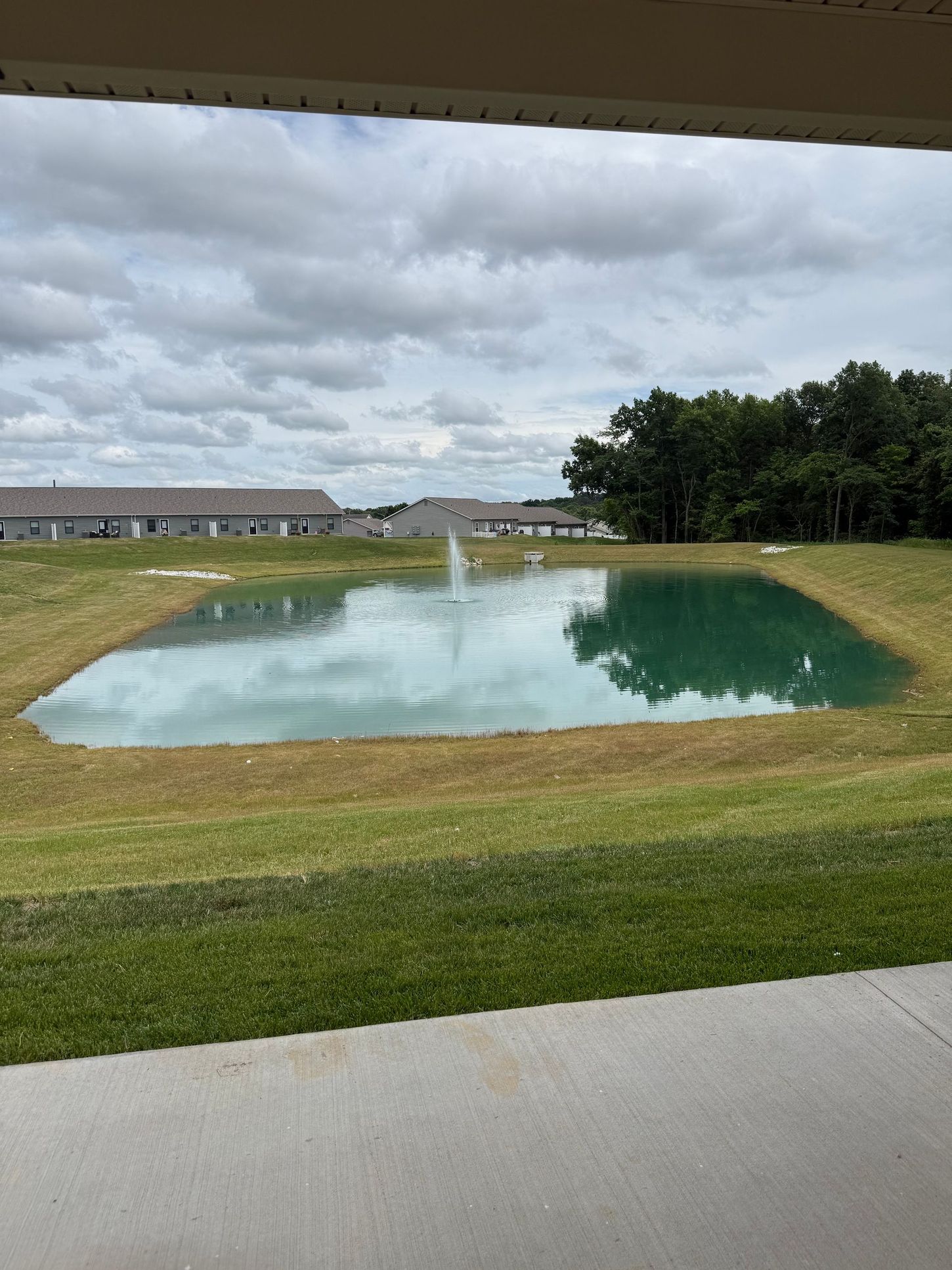 Small pond reflecting cloudy sky beside a grassy field and paved path
