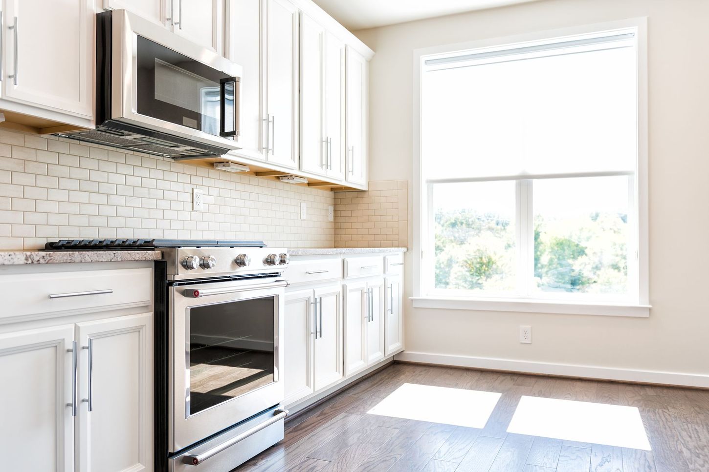 Bright white kitchen with stainless steel appliances, cabinets, and a sunlit window