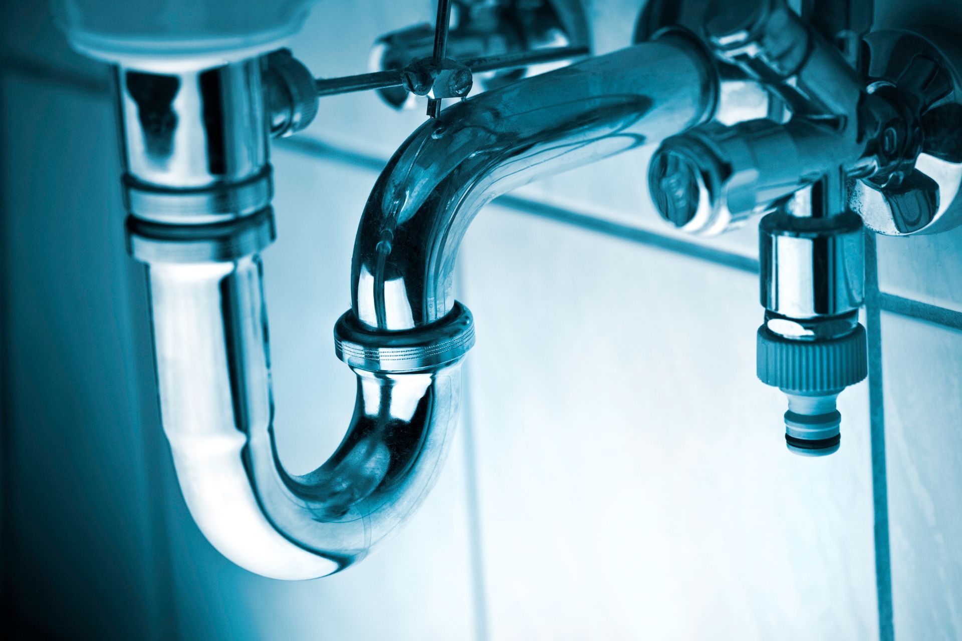 Shiny chrome plumbing under a sink, including a curved pipe and faucet attachments.