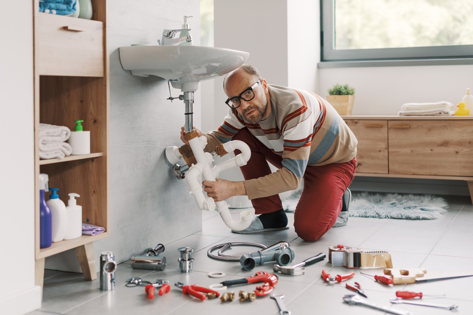 Plumber repairing a bathroom sink, kneeling on the floor with tools scattered nearby. Plumber repairing a bathroom sink, kneeling on the floor with tools scattered nearby.