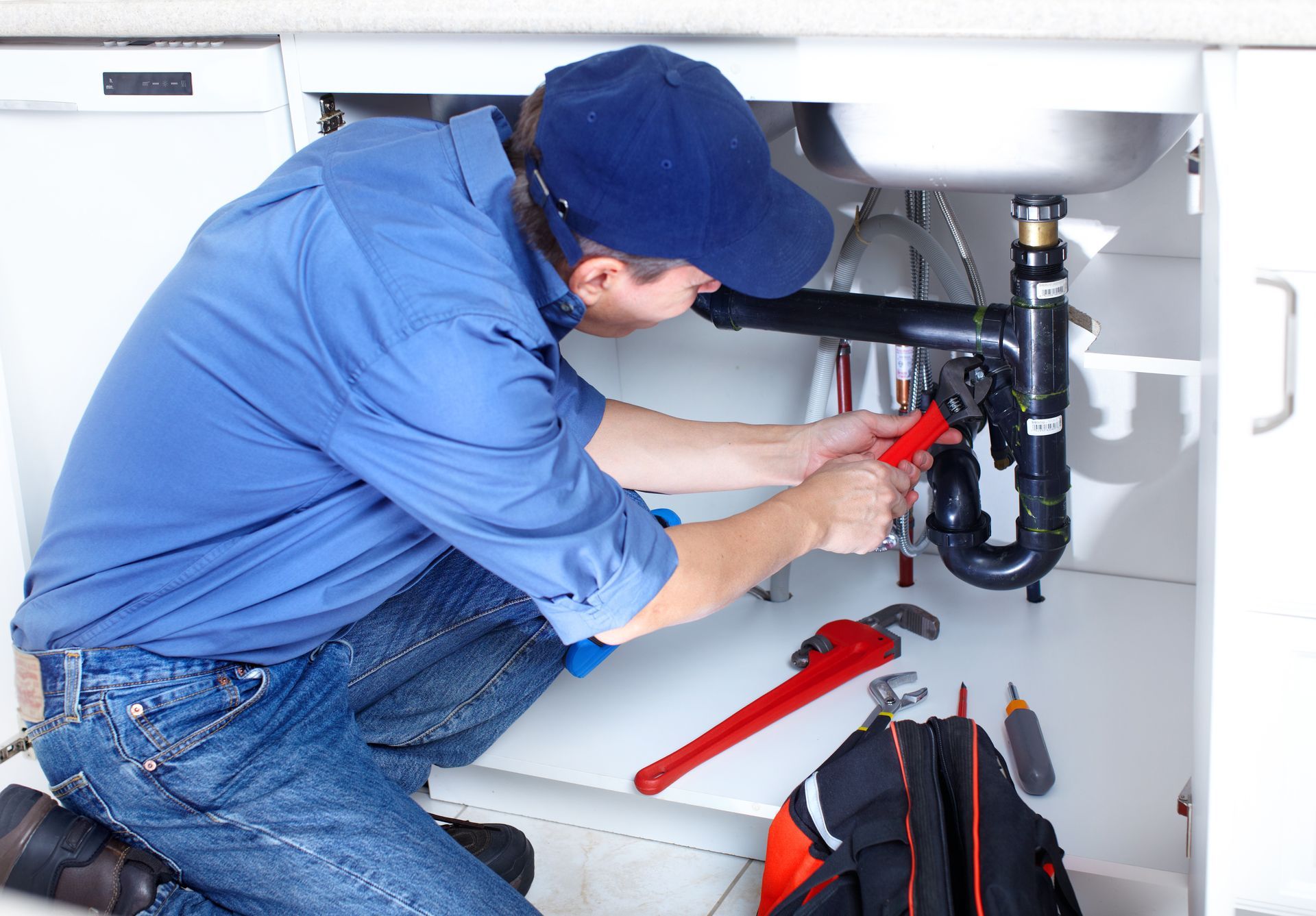 Plumber working under a kitchen sink, tightening pipes with a wrench.