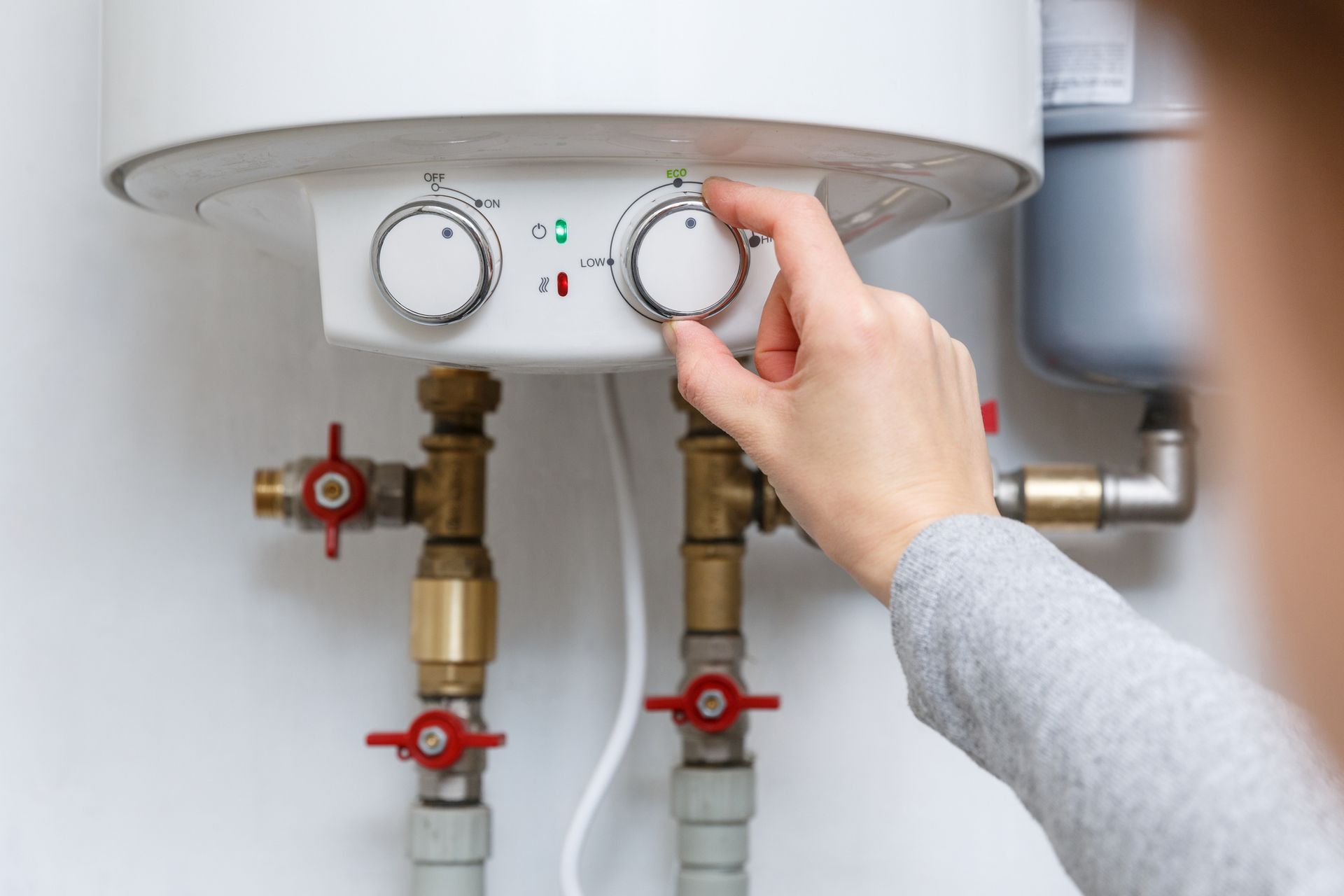 Hand turning a knob on a white water heater, likely adjusting temperature.