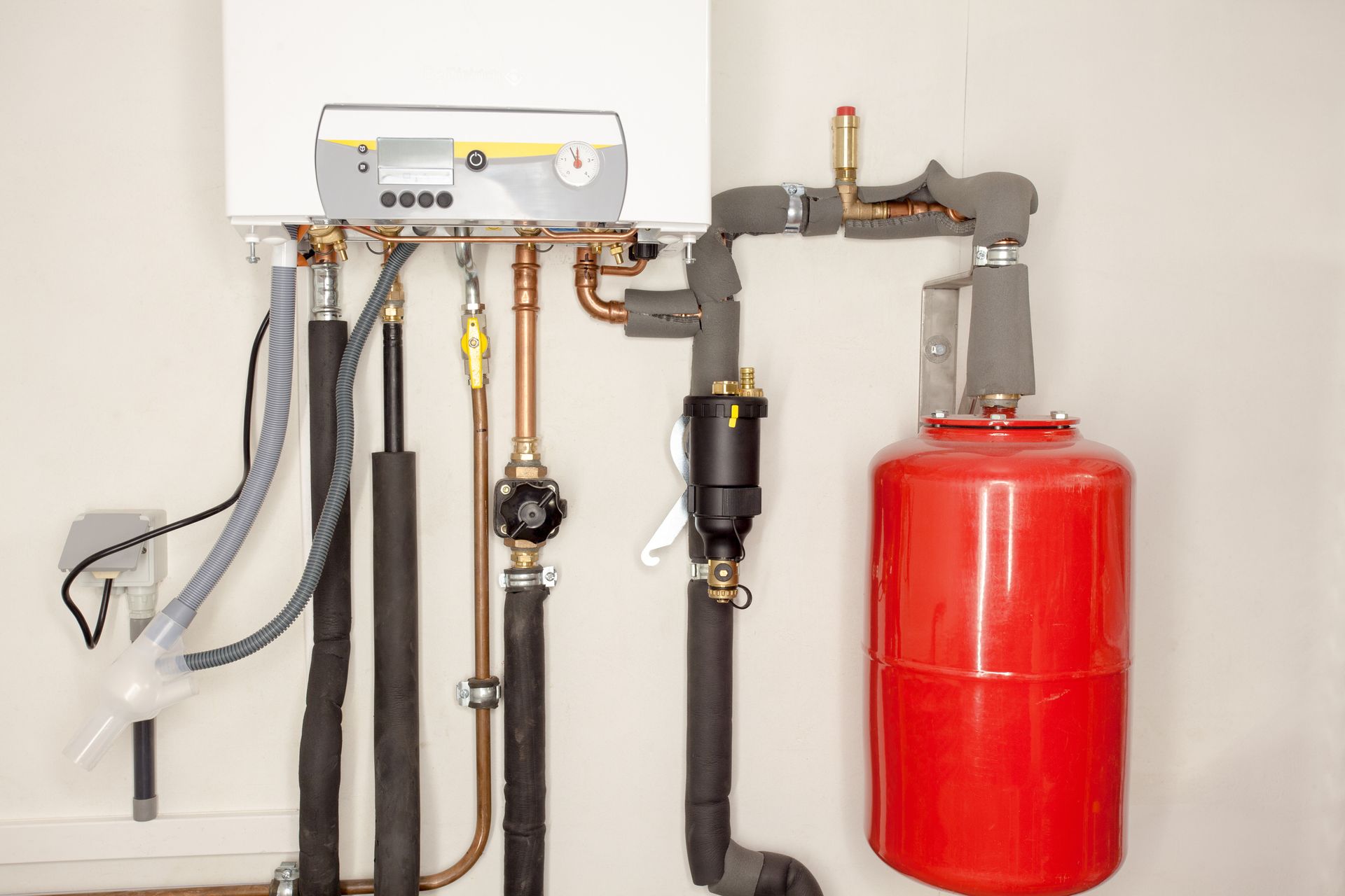 Wall-mounted heating system with pipes, valves, and a red expansion tank against a white wall.