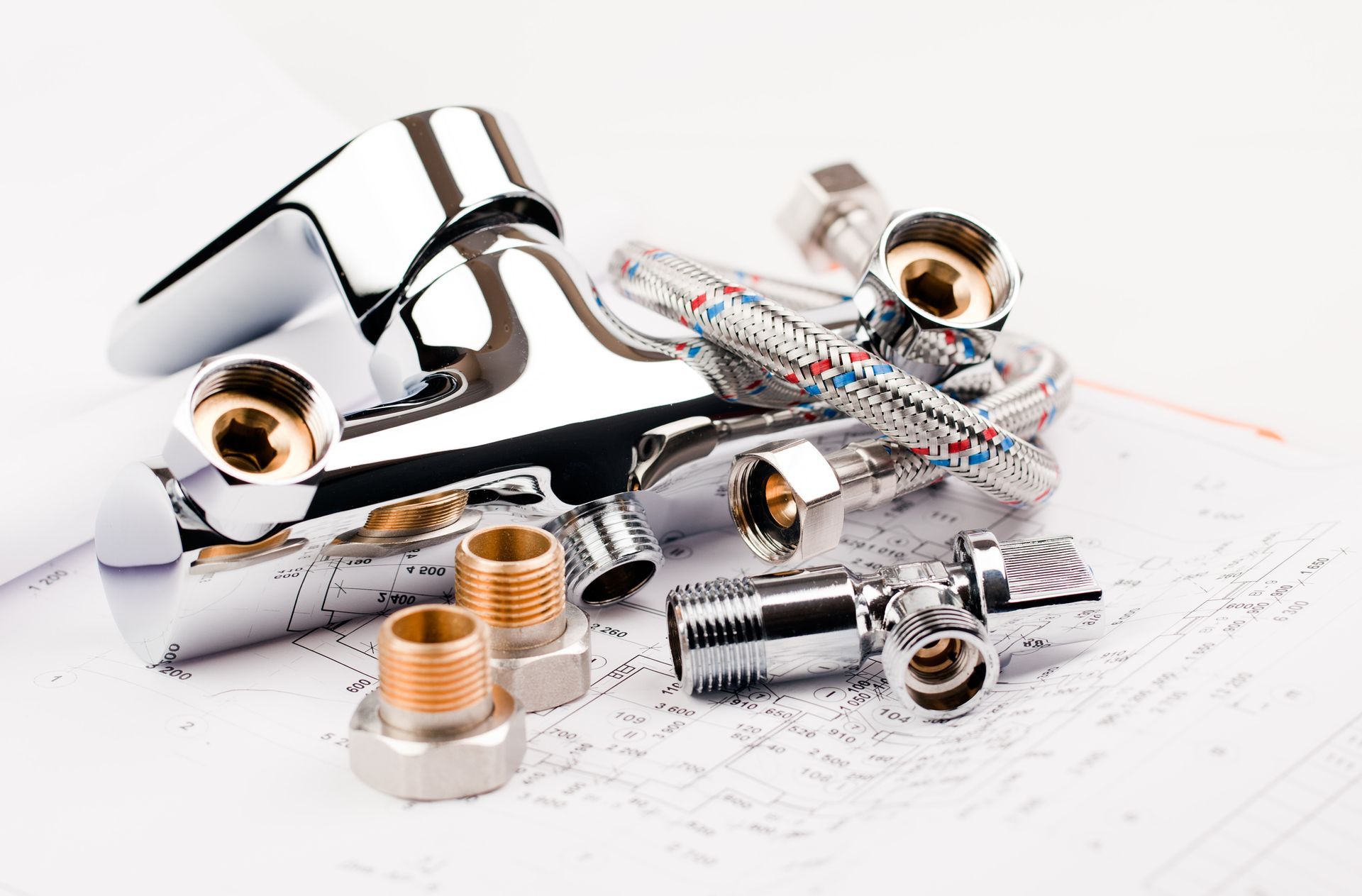 Chrome plumbing fixtures and flexible water supply hoses on architectural blueprints.