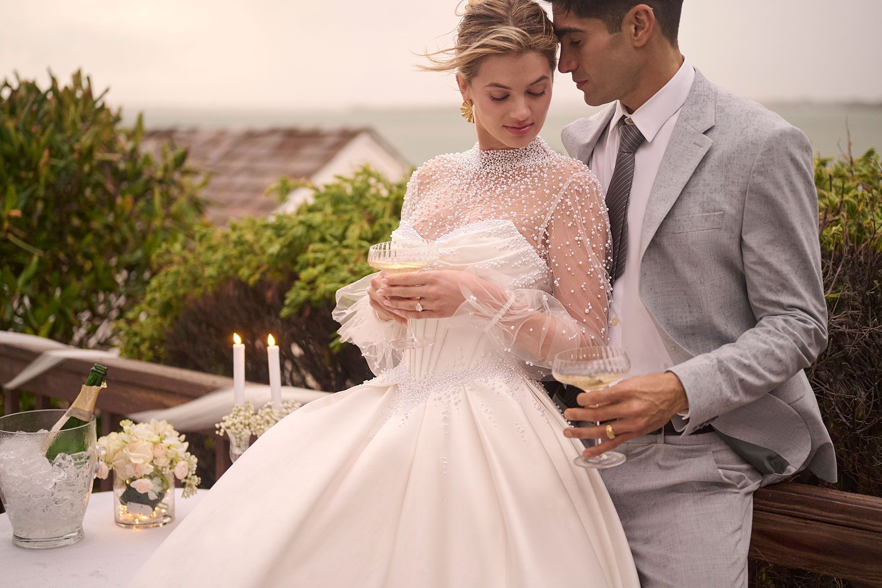 Couple in formal attire toasting with champagne; outdoor setting near the water.