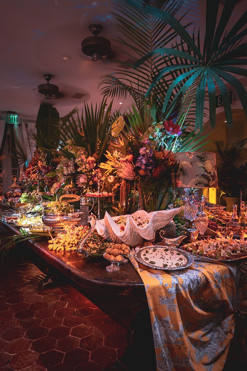 Buffet table laden with food and flowers, illuminated, tropical setting.