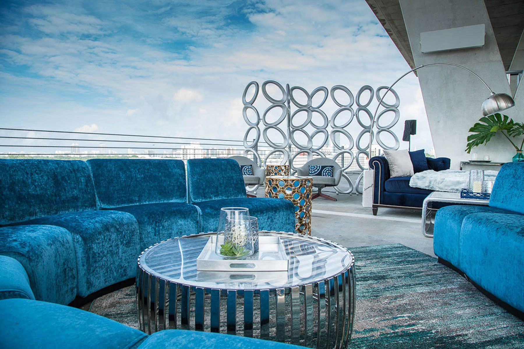 Blue outdoor living room with sofas, round table, metal screen, and ocean view.