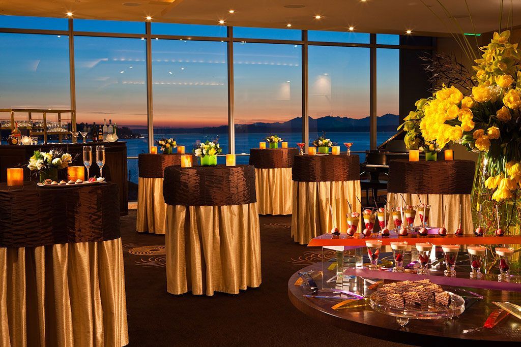 Cocktail reception with round tables, flowers, and sunset views through large windows.