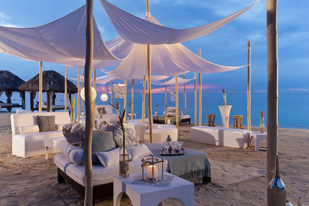 Beach lounge area with white canopy and furniture at dusk.