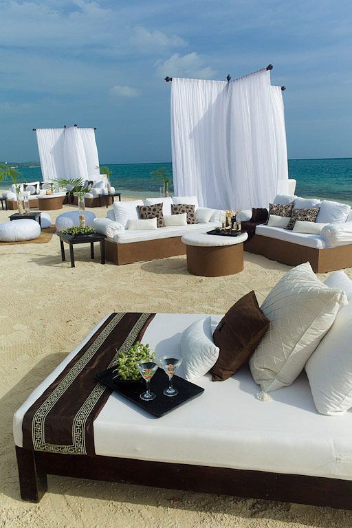 Beach lounge area with white sofas, brown accents, and sheer white curtains, with ocean view.
