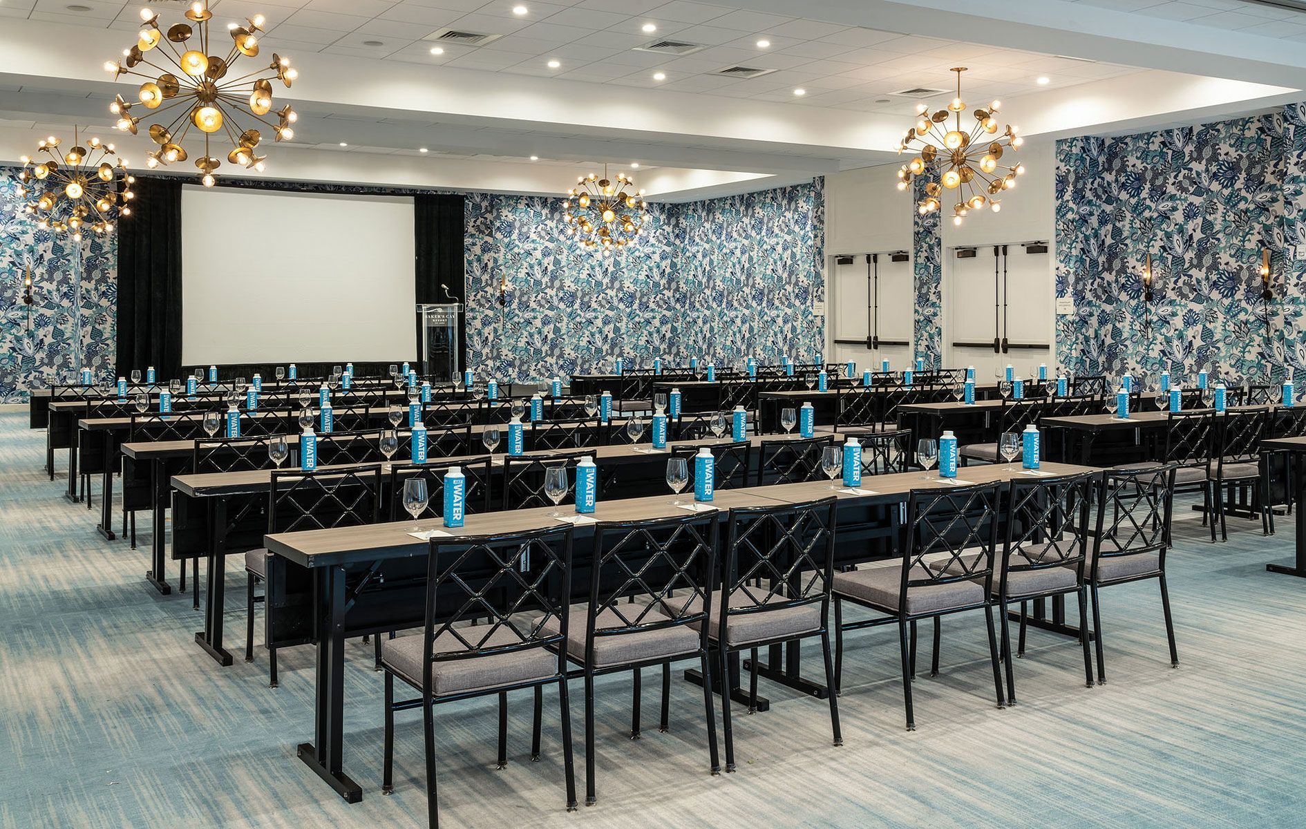 Conference room set for presentation, rows of tables and chairs, projection screen, water bottles, blue and white decor.