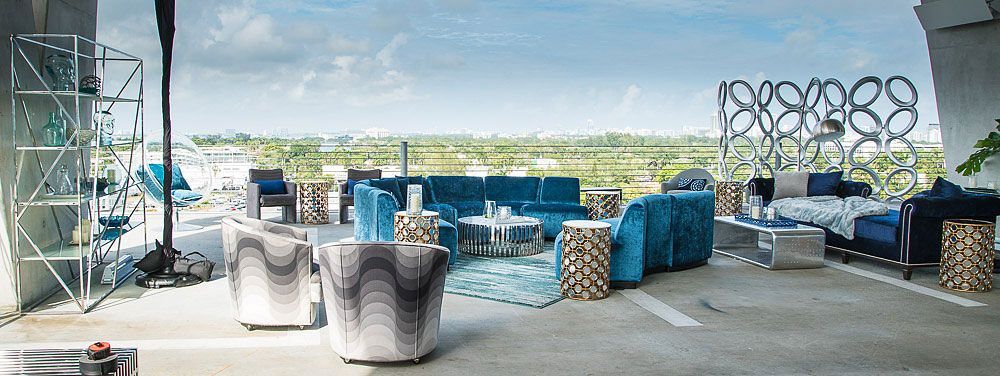 Outdoor patio with blue furniture, rug, and decorative screens, overlooking a green landscape.