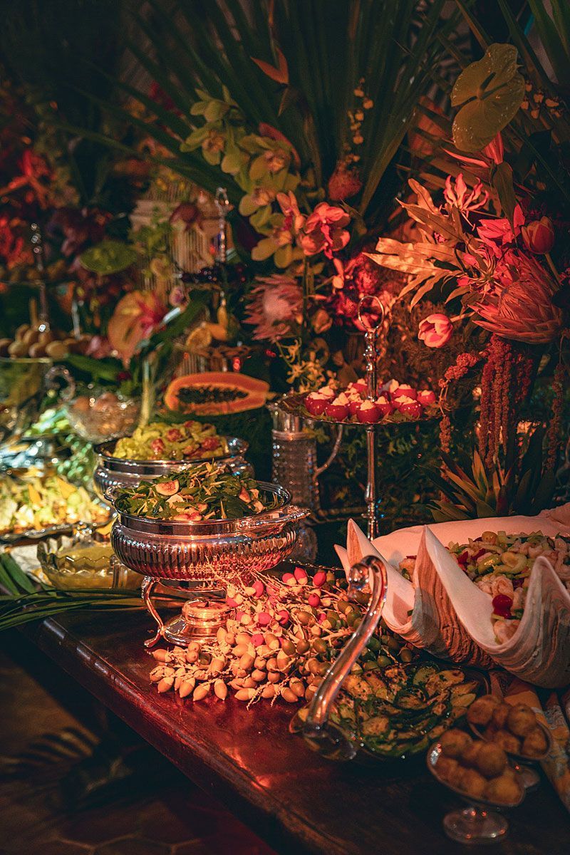 Buffet table laden with food and surrounded by floral arrangements, illuminated by warm lighting.
