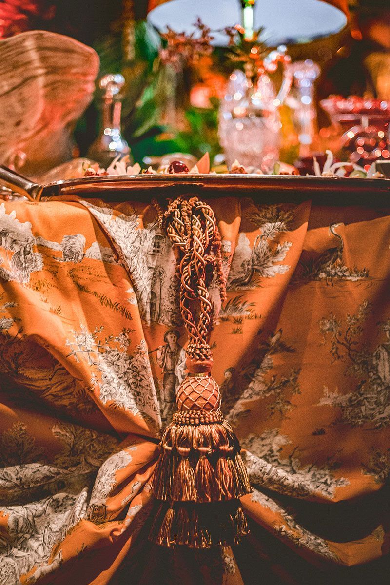 Orange draped buffet table with tassel, displaying food and decorative elements.