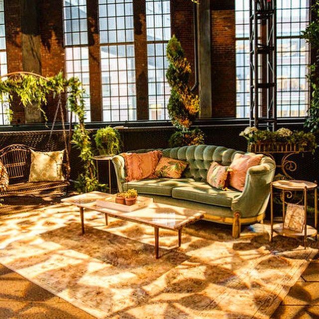 Elegant lounge area with a green sofa, plants, and sunlight streaming through large windows.