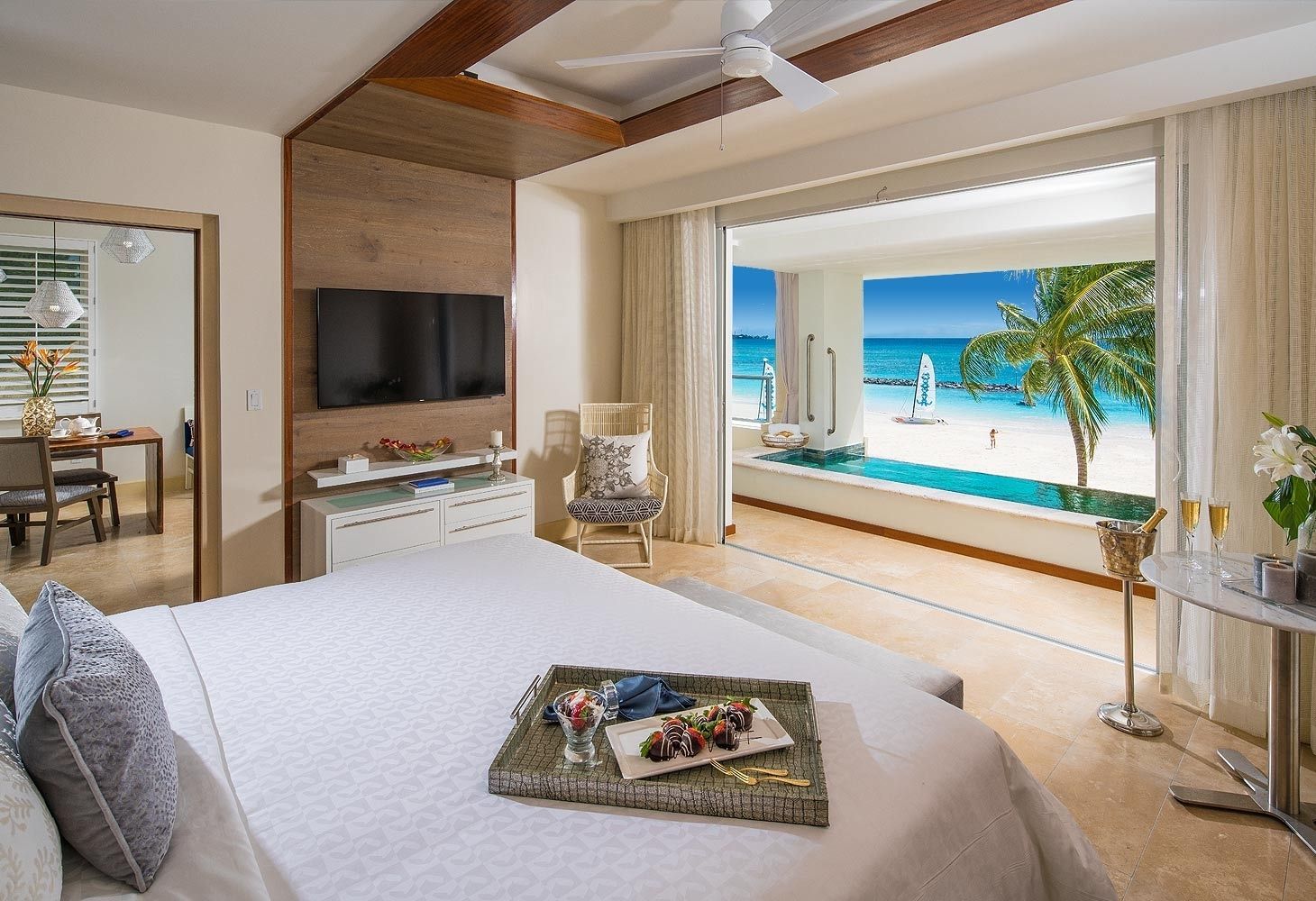 Bedroom with open doors to a beach view and private pool, featuring a large bed and a dining area.