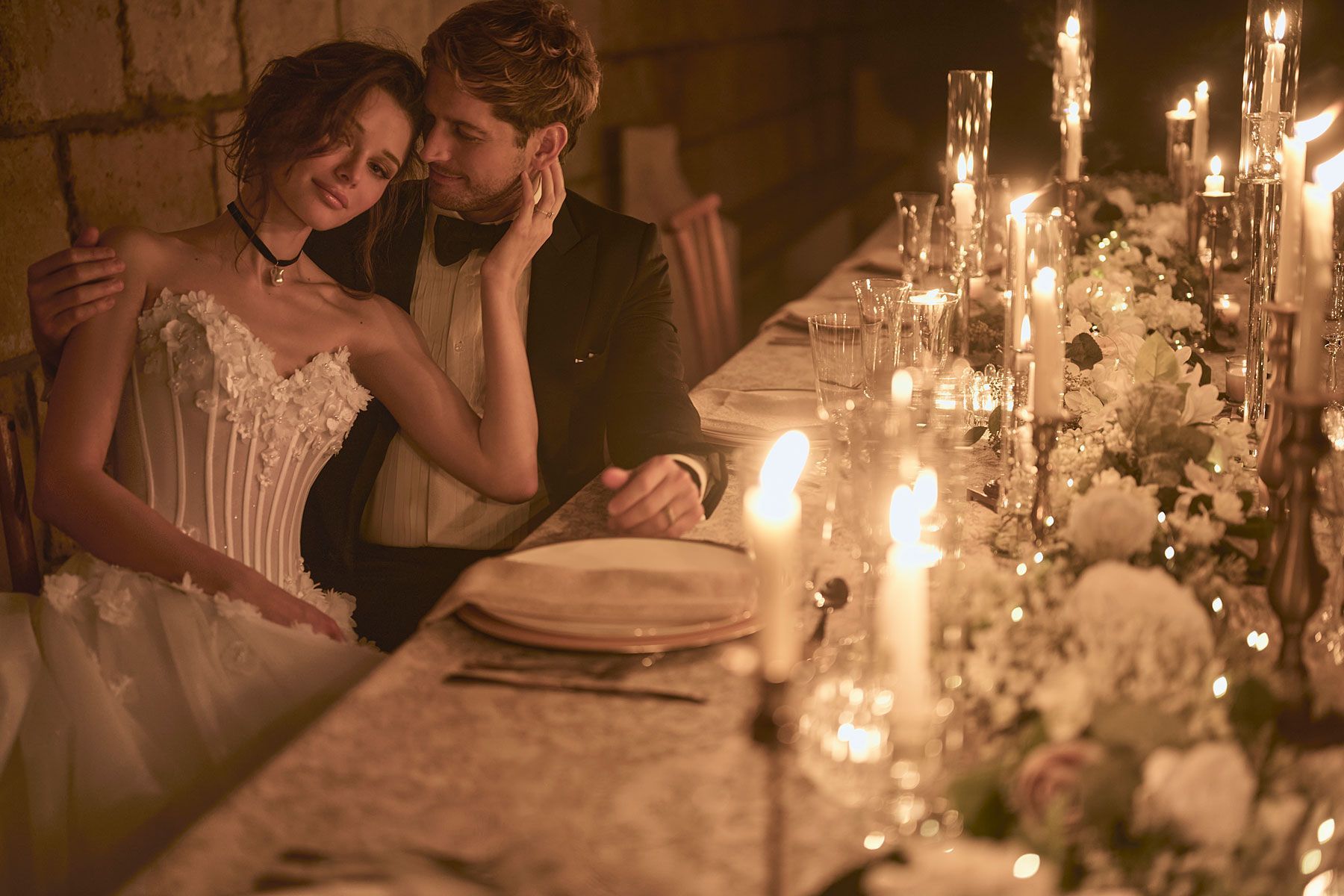 Couple at a candlelit dinner, woman in a white dress, man in a tuxedo, romantic atmosphere.