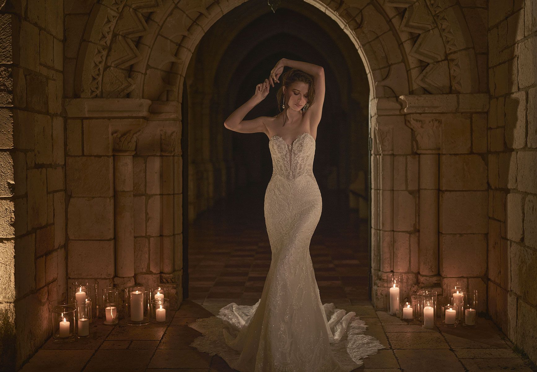 Woman in a white wedding dress poses in a stone archway lit by candles.