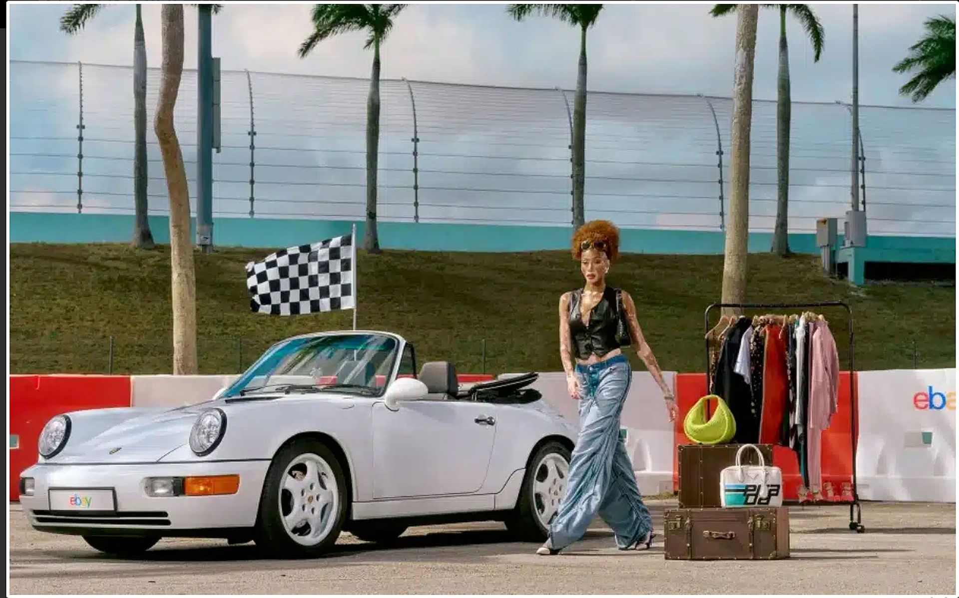 White convertible car with a person in front of clothes rack at a racetrack.