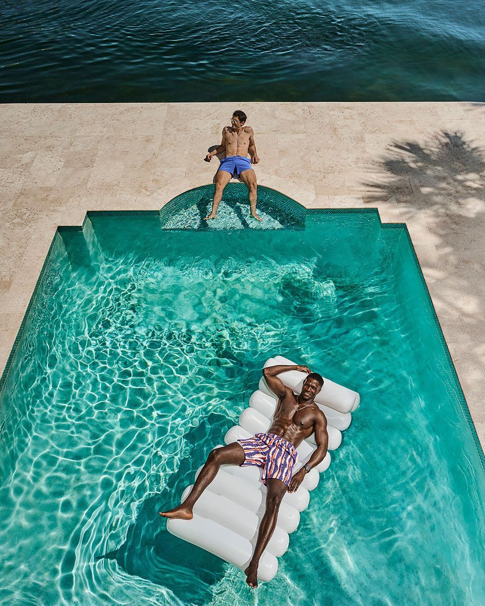 Two people enjoying a pool on a sunny day. One relaxes on a raft, the other sits on a pool edge.