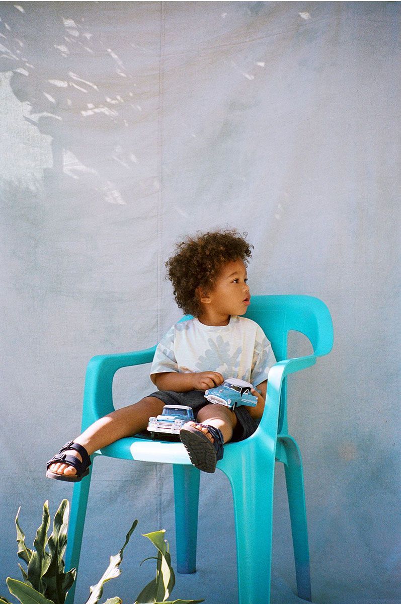 Boy sitting on a turquoise chair, playing with toy cars outside.
