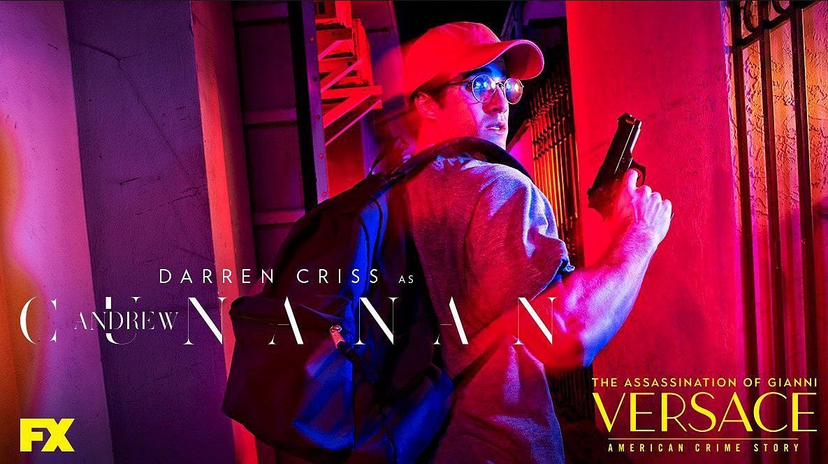 Man in red cap and glasses holds a gun, lit by red and blue light. 