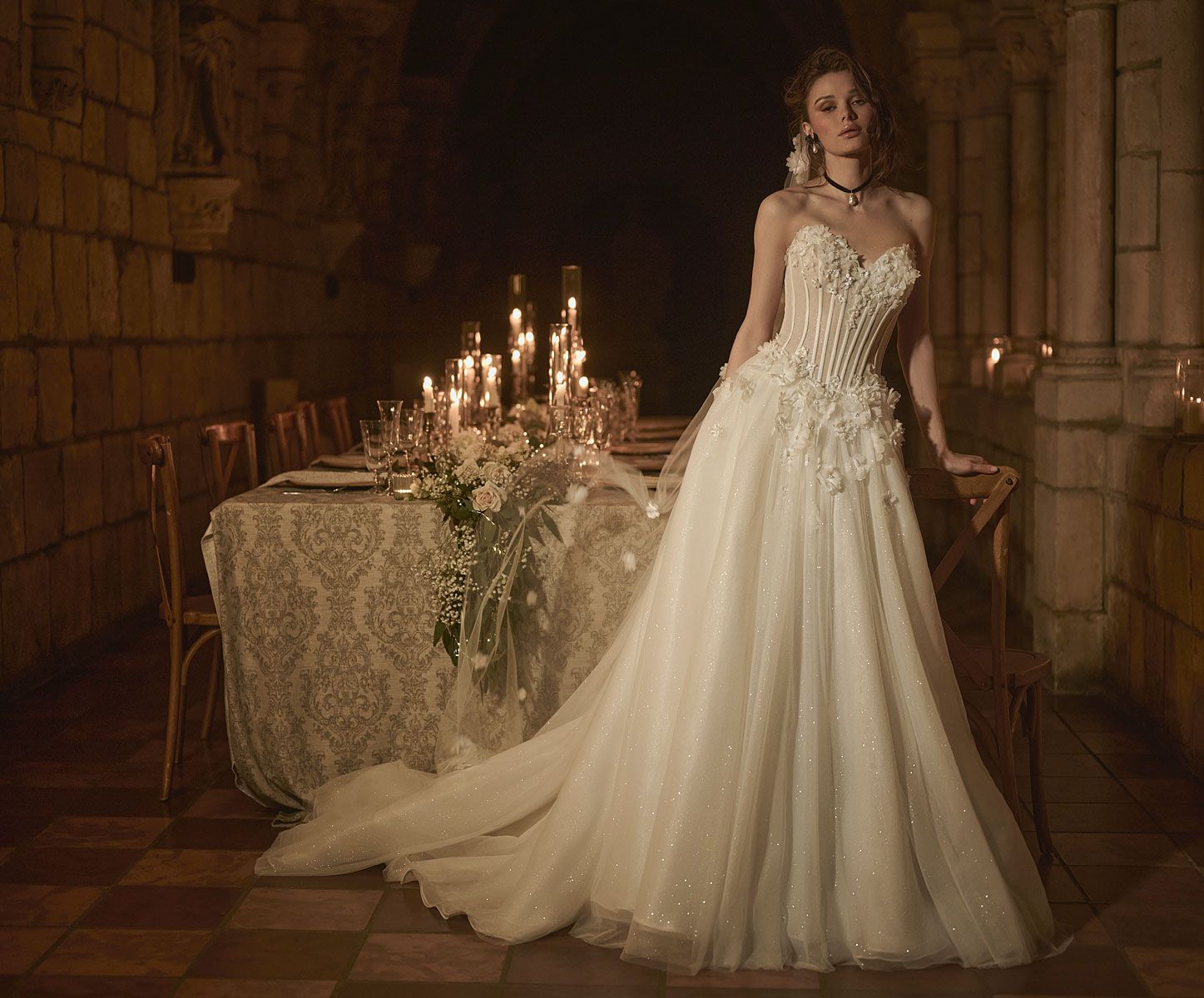 Woman in a white wedding gown leans by a table set for a candlelit dinner.