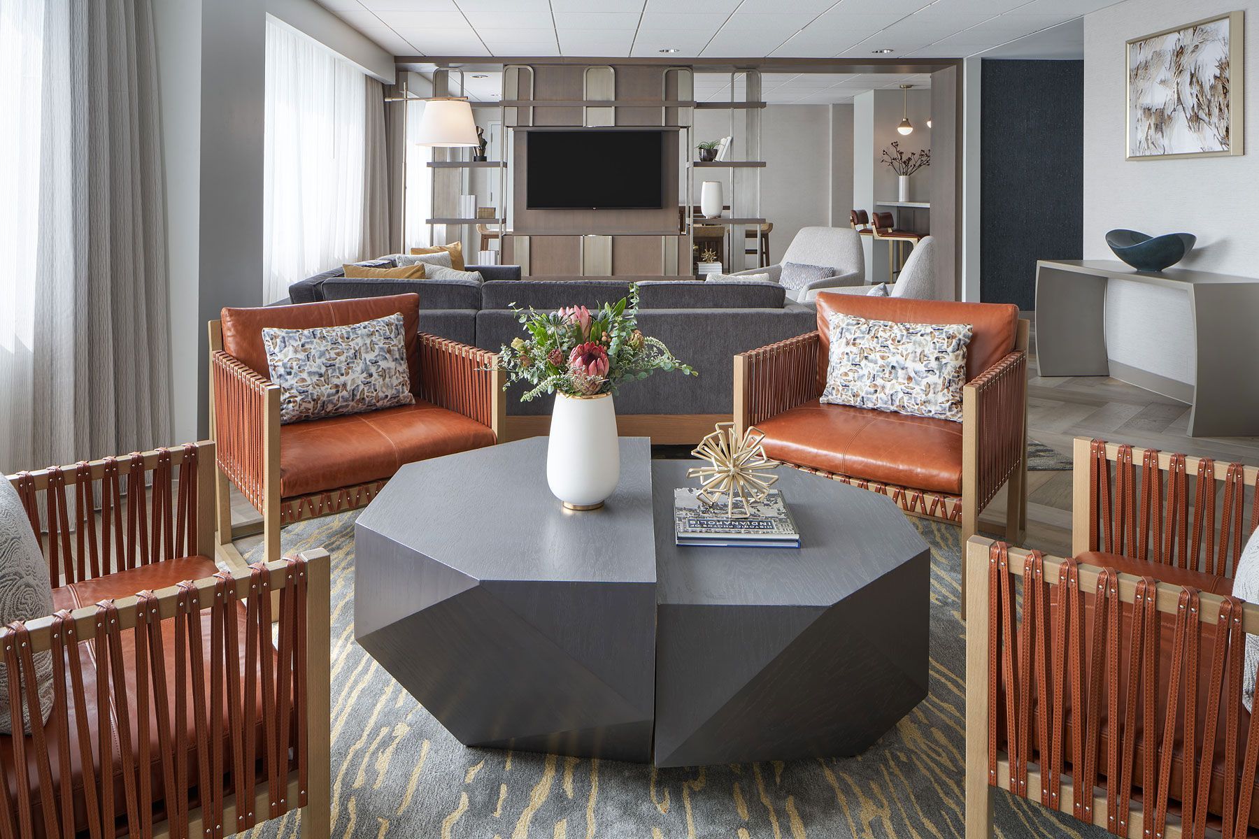 Cozy living room with orange chairs, gray geometric coffee table, and floral arrangement. Neutral color palette.
