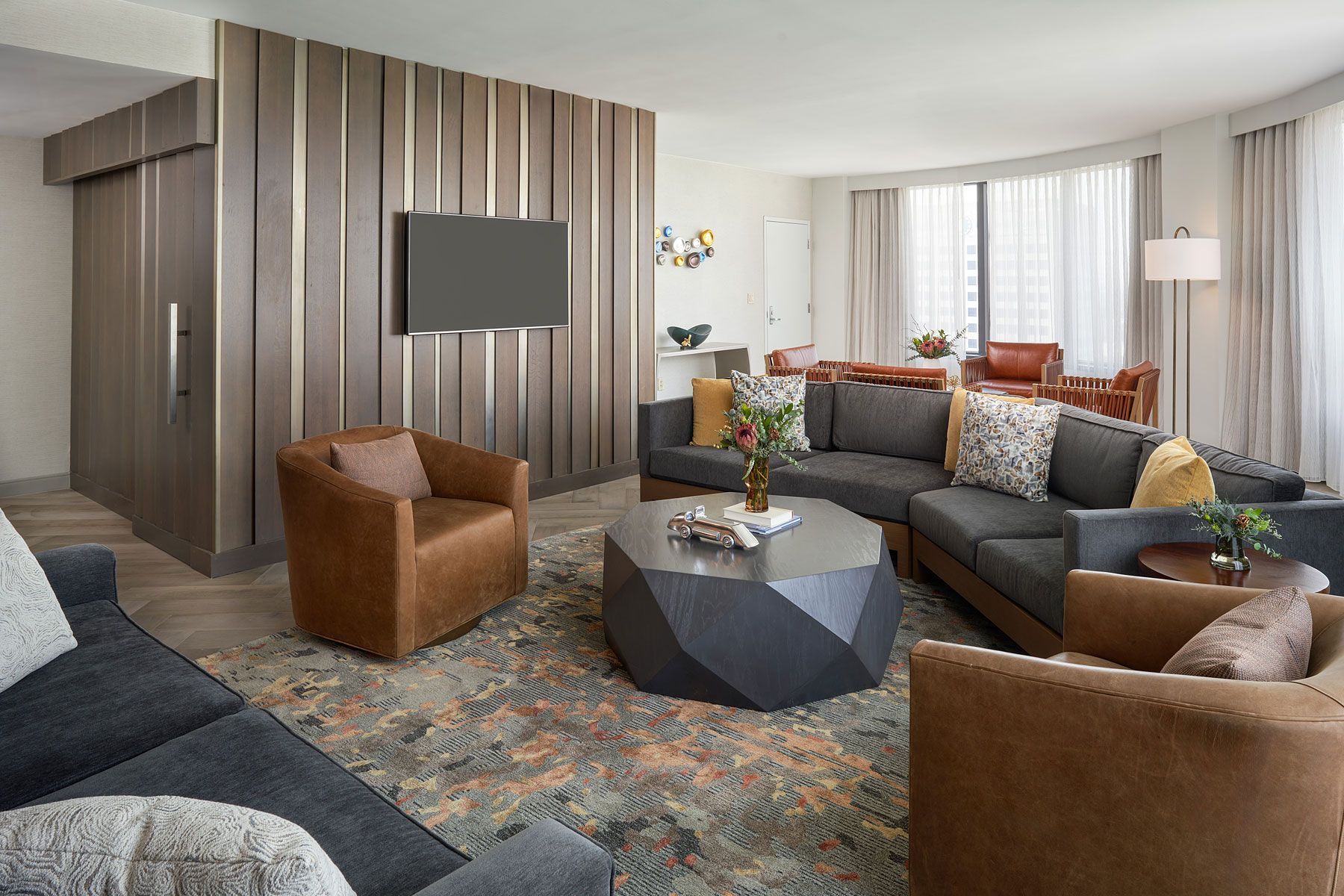 Modern living room with sectional sofa, brown chairs, geometric coffee table, and large window.