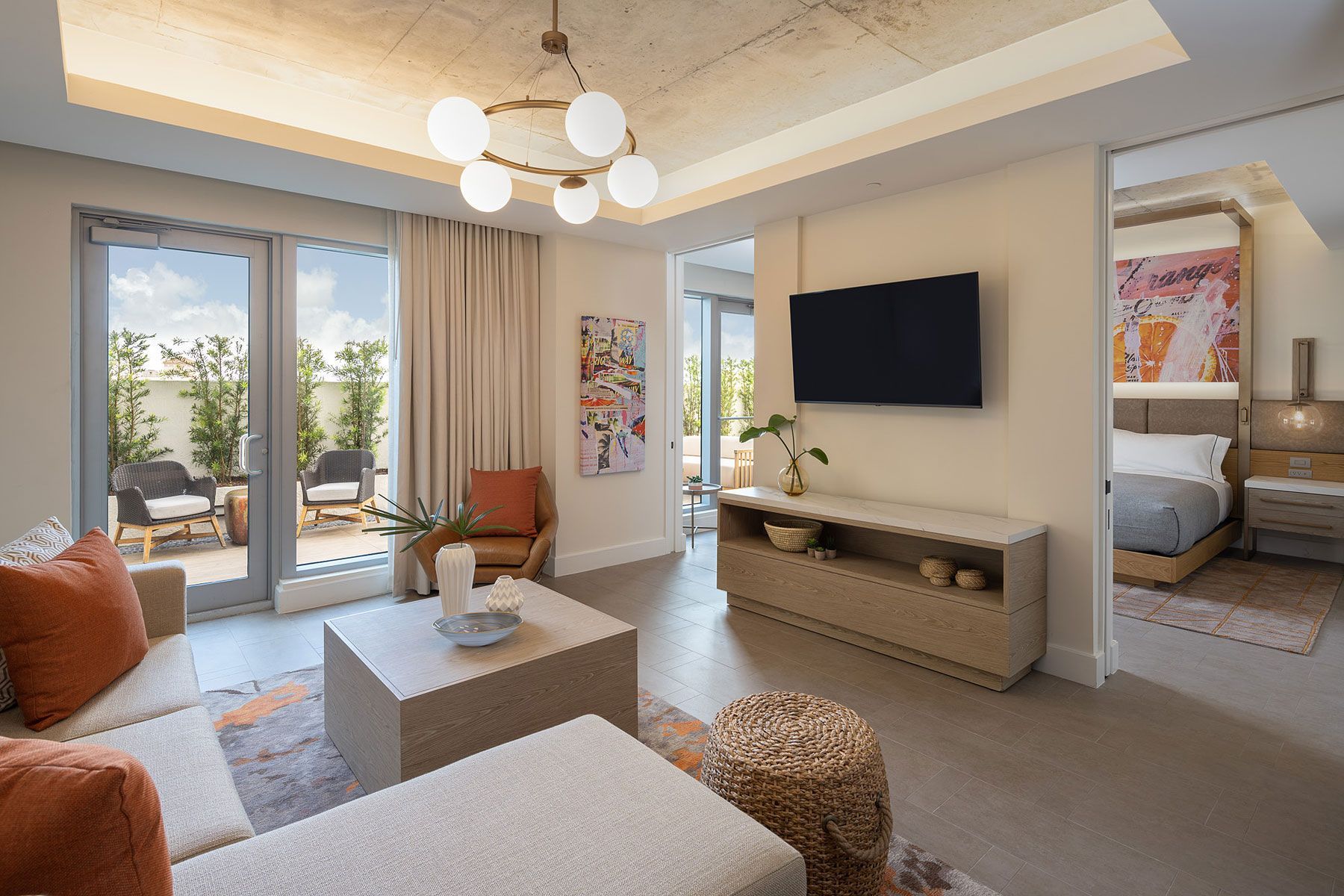 Modern living room with open doors to a patio. Includes a sofa, TV, and view into the bedroom.