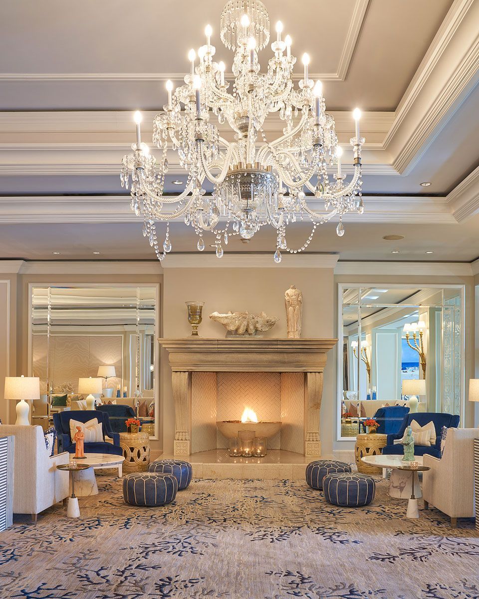 Elegant hotel lounge with a crystal chandelier, fireplace, mirrors, seating, and patterned rug.