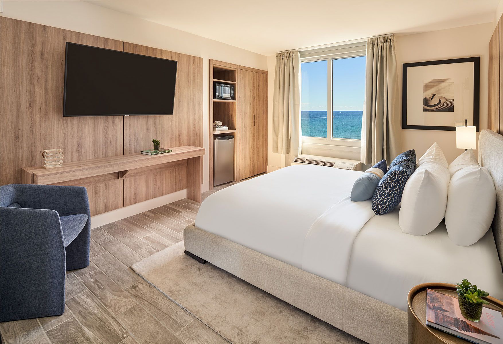 Hotel room with a bed, ocean view, TV, and wooden paneling.