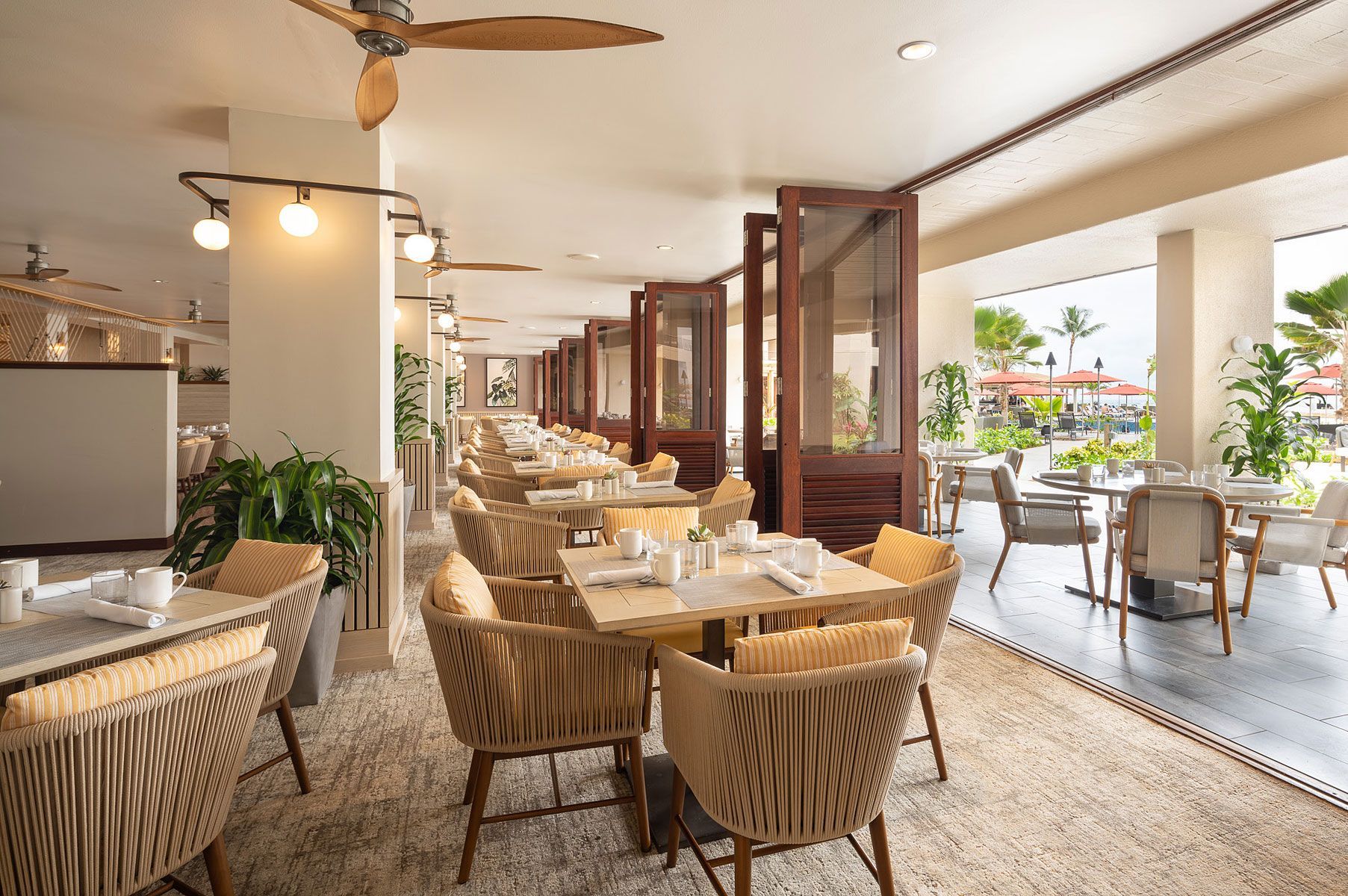 Outdoor restaurant with woven chairs, tables, and wooden dividers; cream and natural tones.