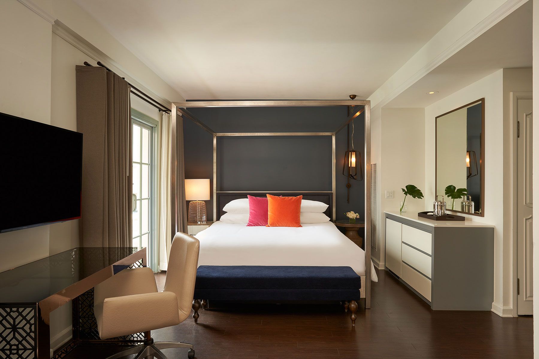 Bedroom with a four-poster bed, desk, and dresser. Dark walls, white trim, and a blue bench.