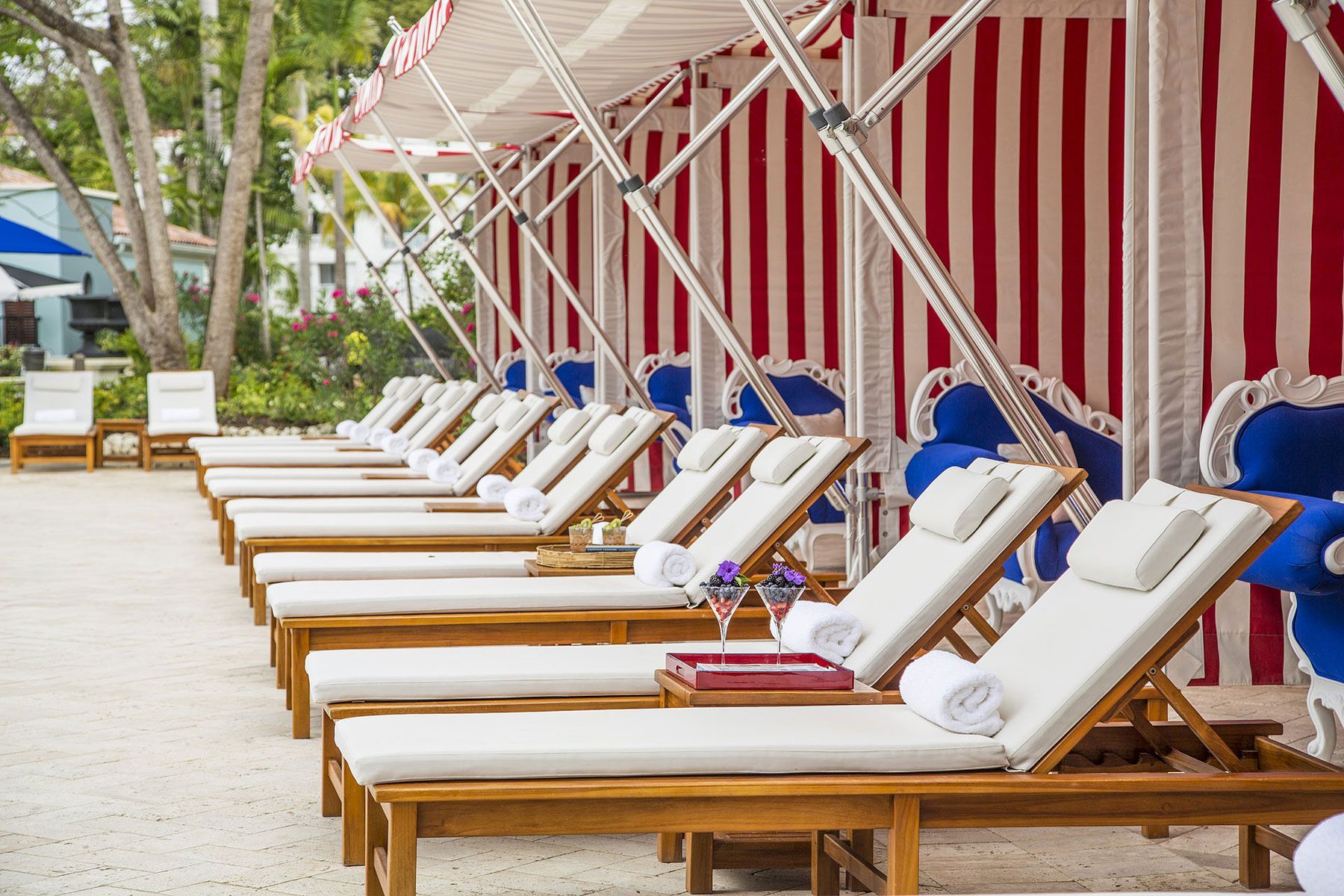 Lounge chairs lined up under a red and white striped awning near a pool.