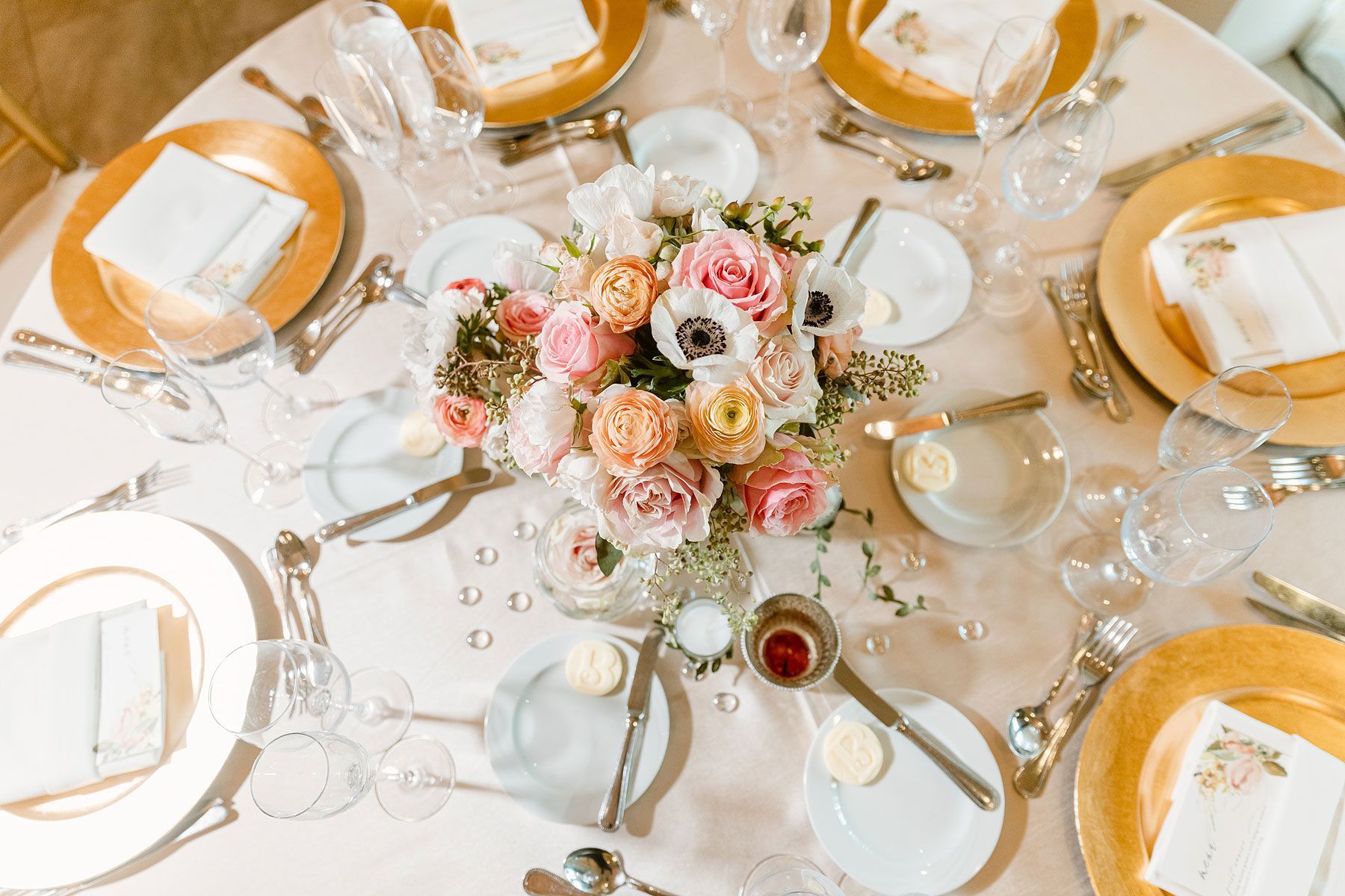 Elegant table setting with gold-rimmed plates, flowers, and white linens for a formal event.
