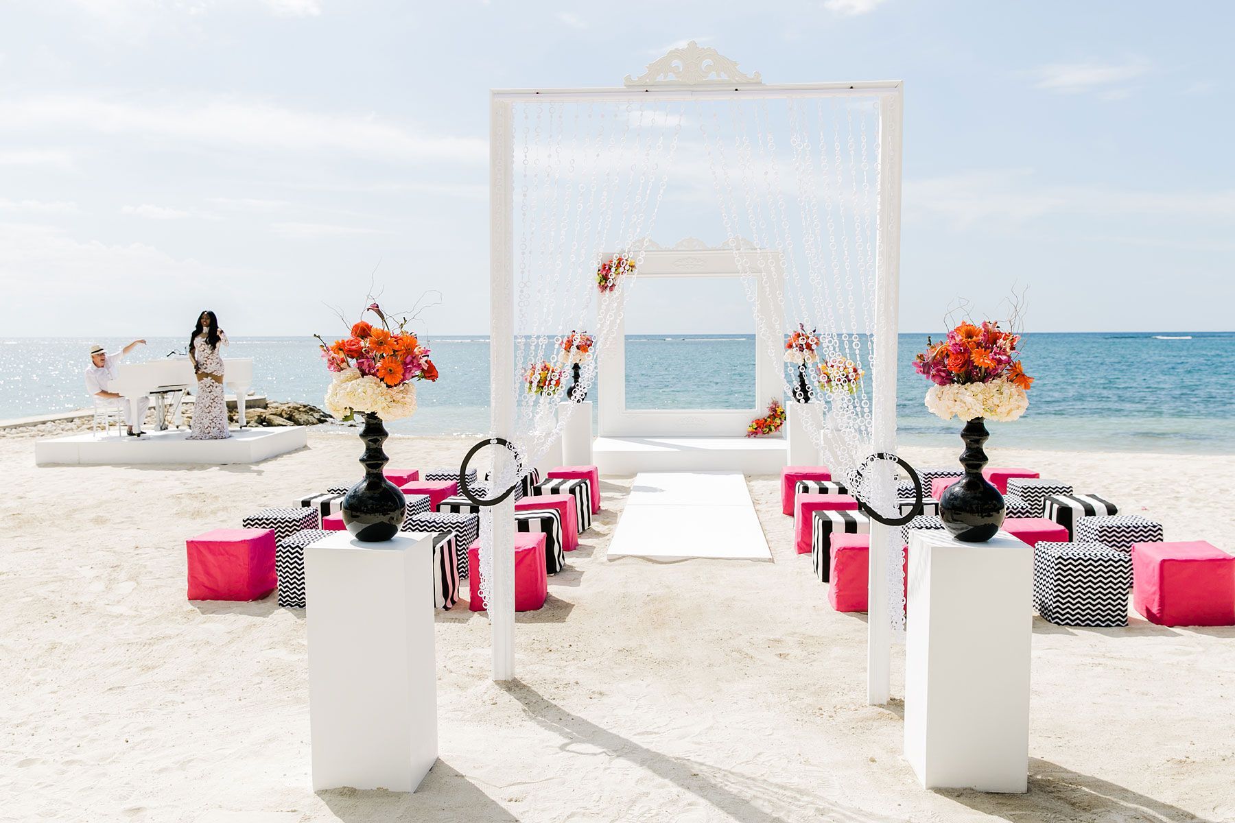 Beach wedding setup with white altar, floral arrangements, and seating; ocean in background.