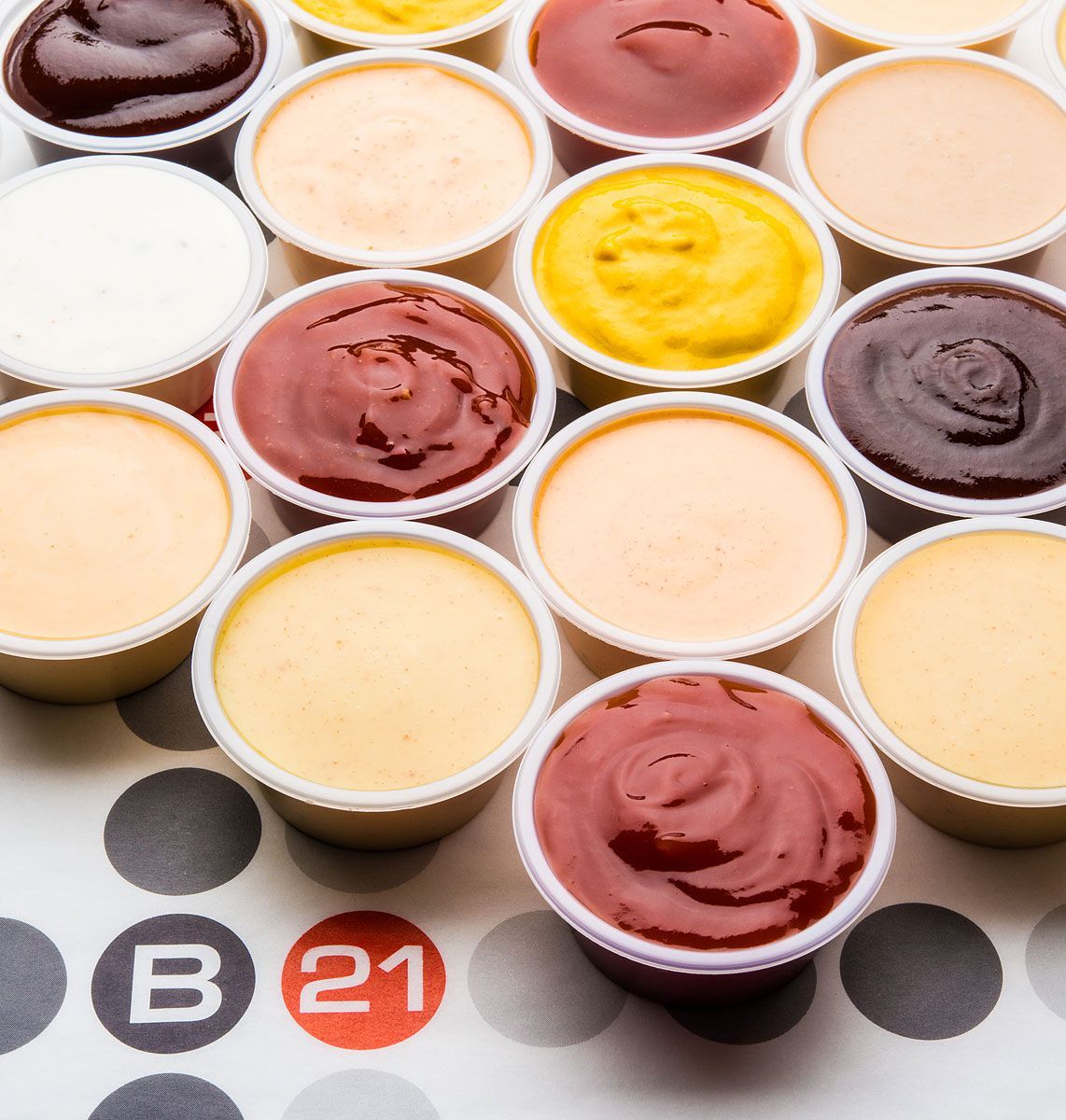 Small plastic cups filled with various colorful sauces arranged on a polka dot surface,