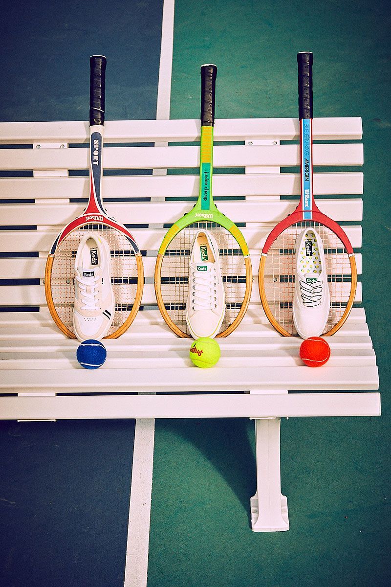Three tennis rackets with sneakers and balls on a white bench, set against a green court.