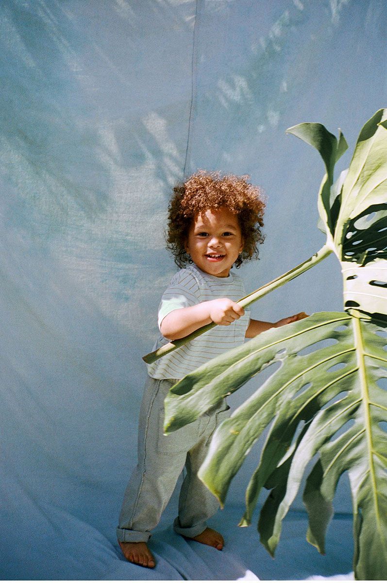 Child with curly hair holding a plant stem, smiling in front of a blue backdrop.