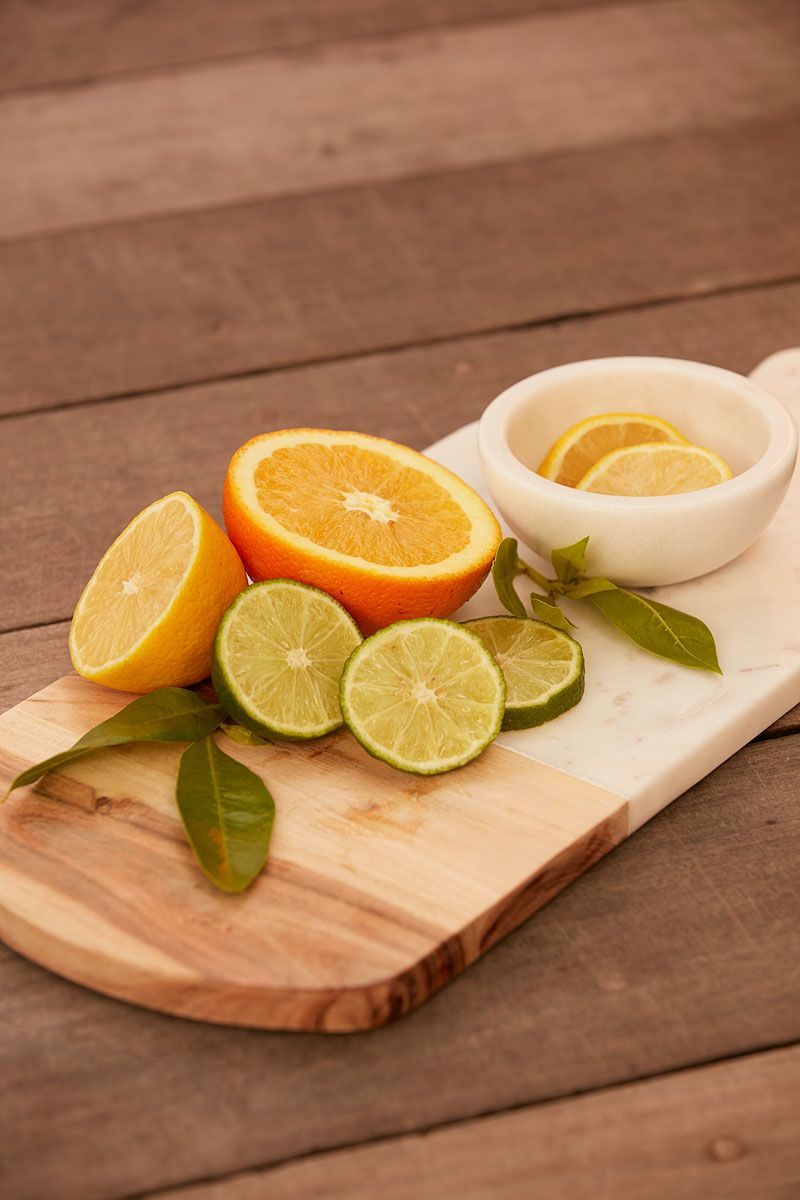 Citrus fruits (orange, lime, lemon) on a wooden cutting board with a small bowl of lemon slices.