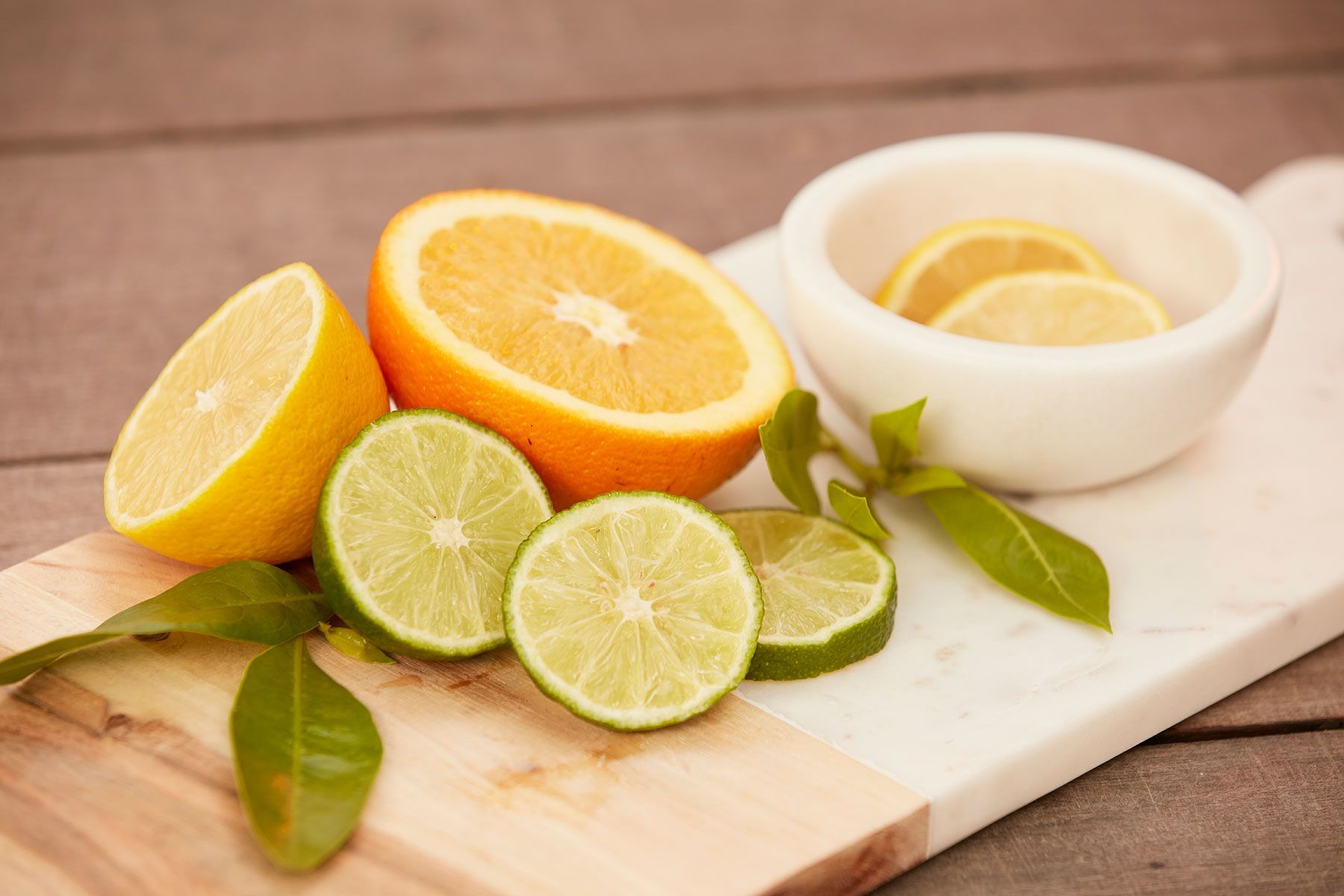 Sliced citrus fruits (orange, lemon, lime) and lemon slices in a bowl on a wooden board.
