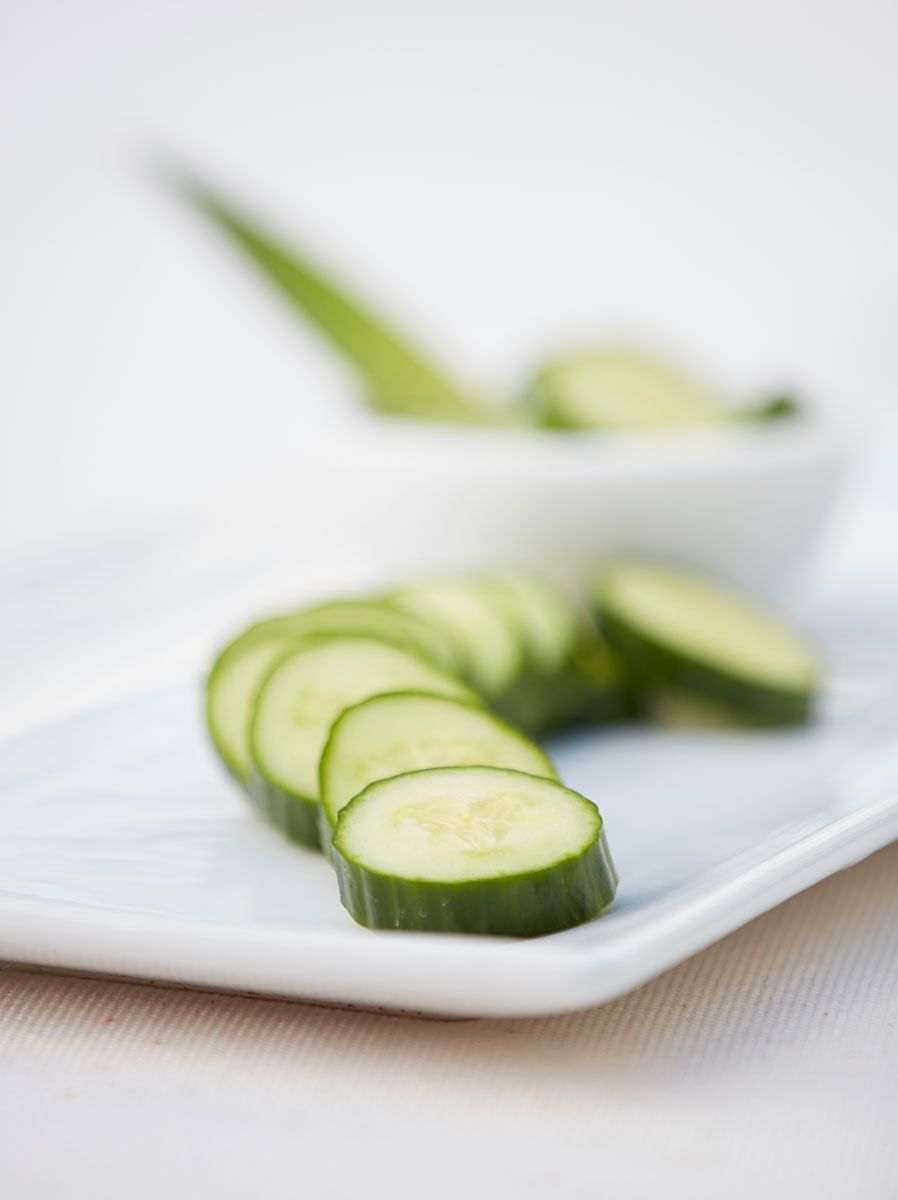 Sliced cucumbers on a white plate, with more in a bowl in the background.