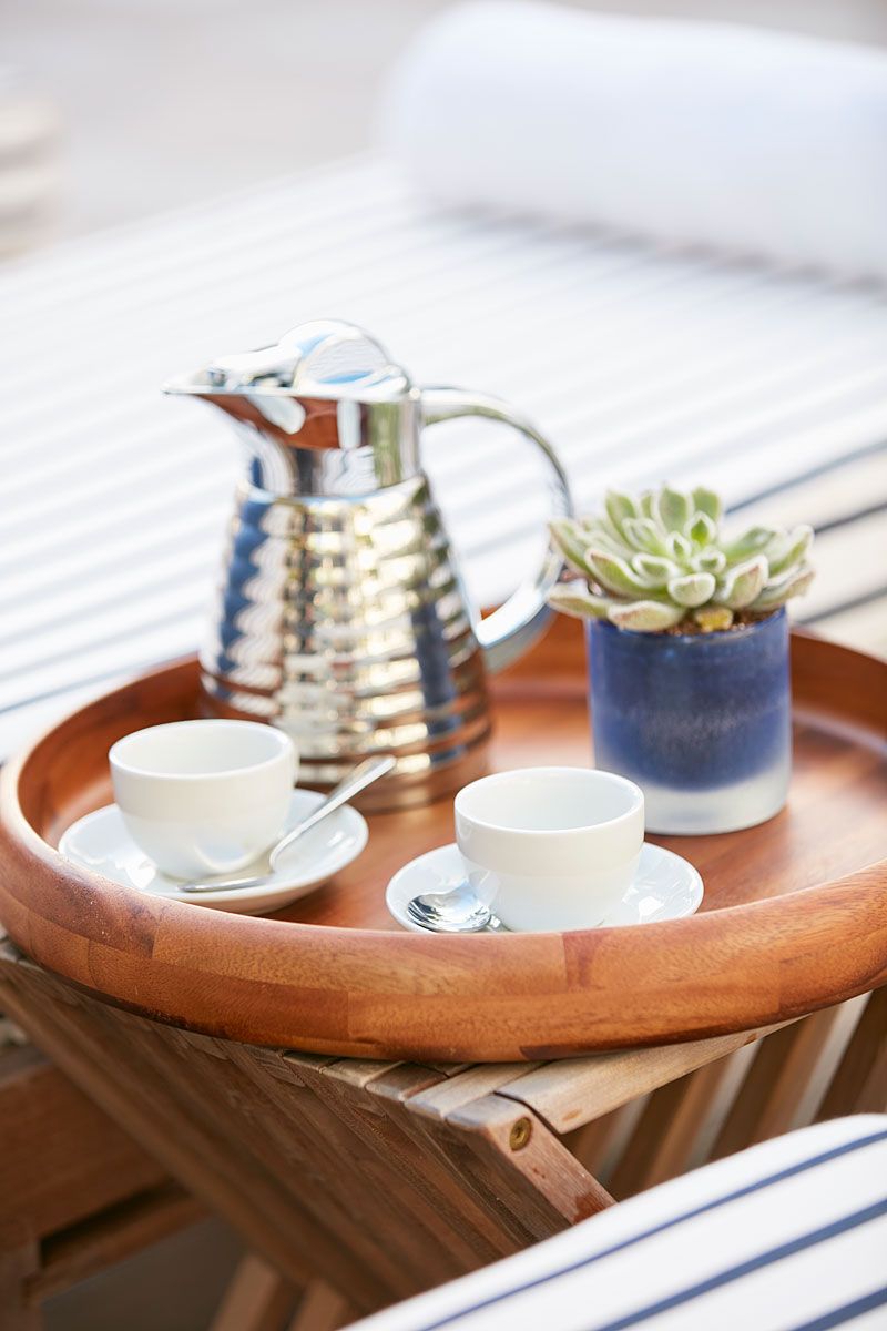 Wooden tray with coffee service and succulent plant on striped lounge chair.