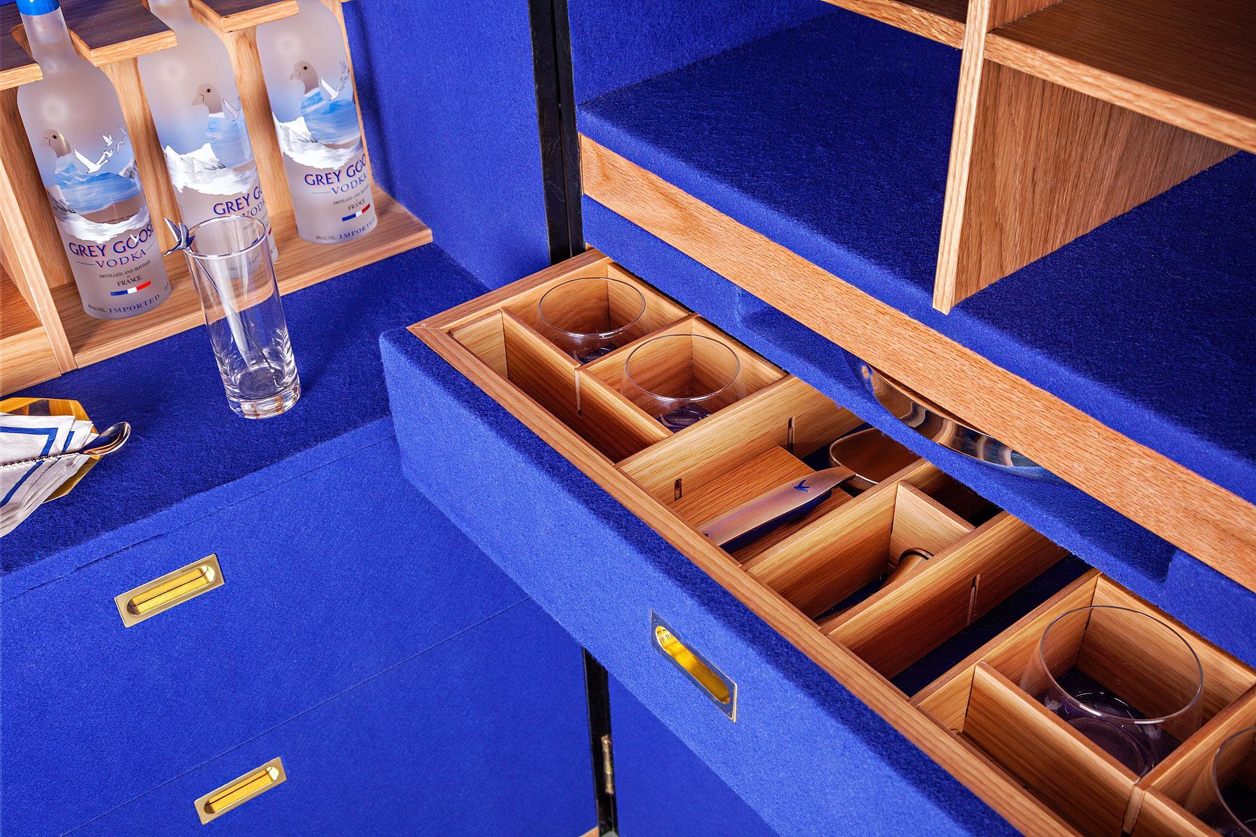 Close-up of a blue and wood bar cabinet with bottles, glasses, and drawers.